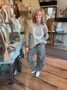 Lu in her boutique in Leavenworth, KS wearing a beige sweater with a white horseshoe design and leopard print barrel pants.
