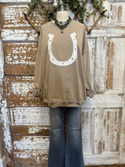 Taupe long-sleeve top with a horseshoe design on a mannequin against a rustic wooden background.
