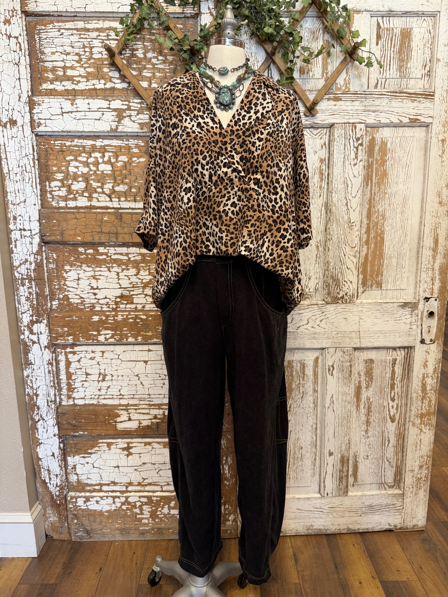 Mannequin wearing a leopard print collared top with handmade turquoise jewelry and blue jeans against a rustic wooden background