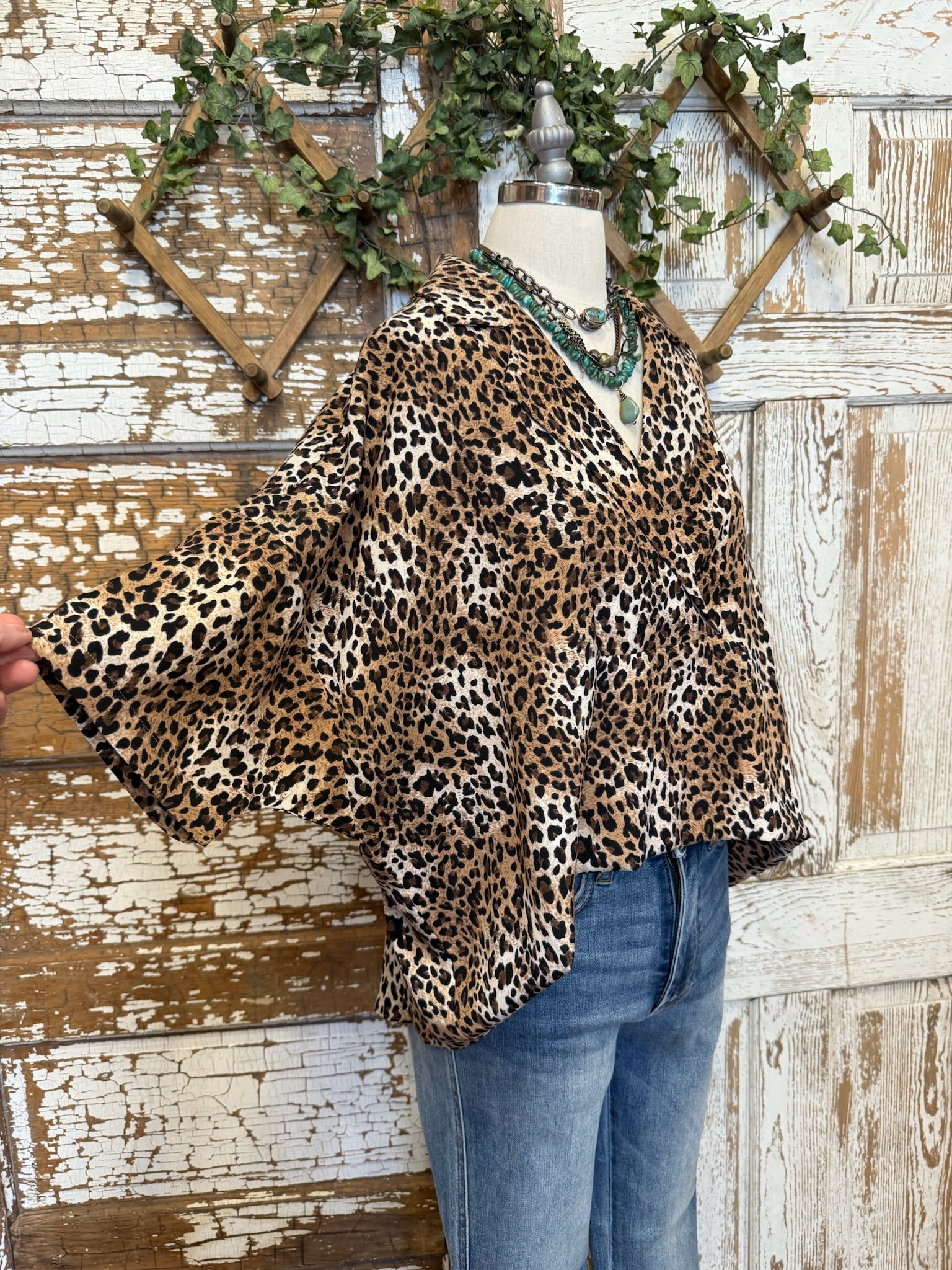 Mannequin wearing a leopard print collared top with handmade turquoise jewelry and blue jeans against a rustic wooden background