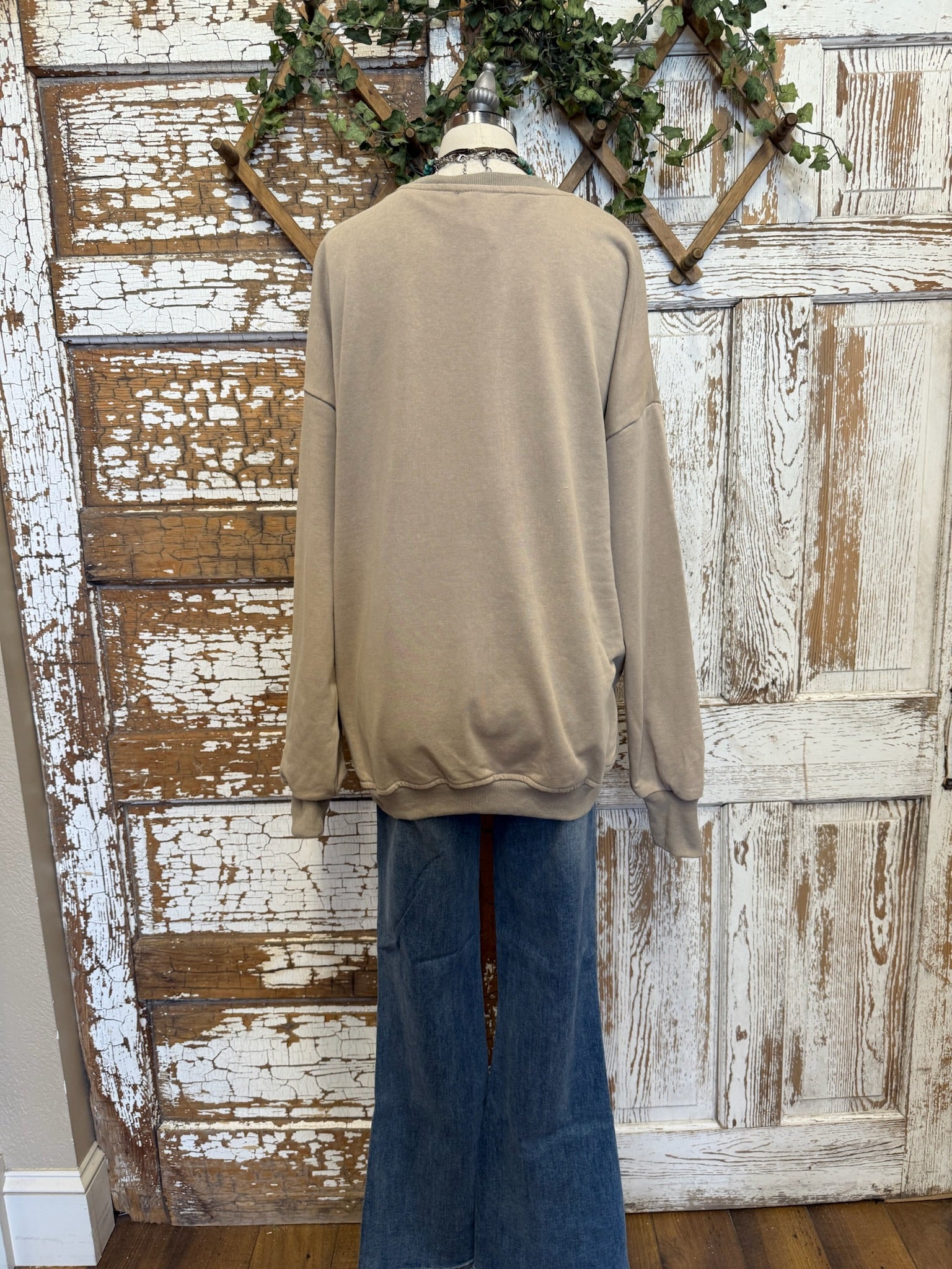 Beige sweater on a mannequin against a rustic wooden wall.