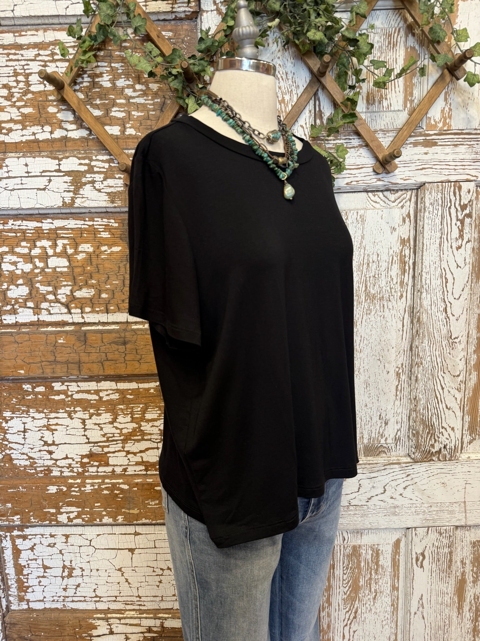 Black top and handmade jewelry worn by a mannequin against an artistic background