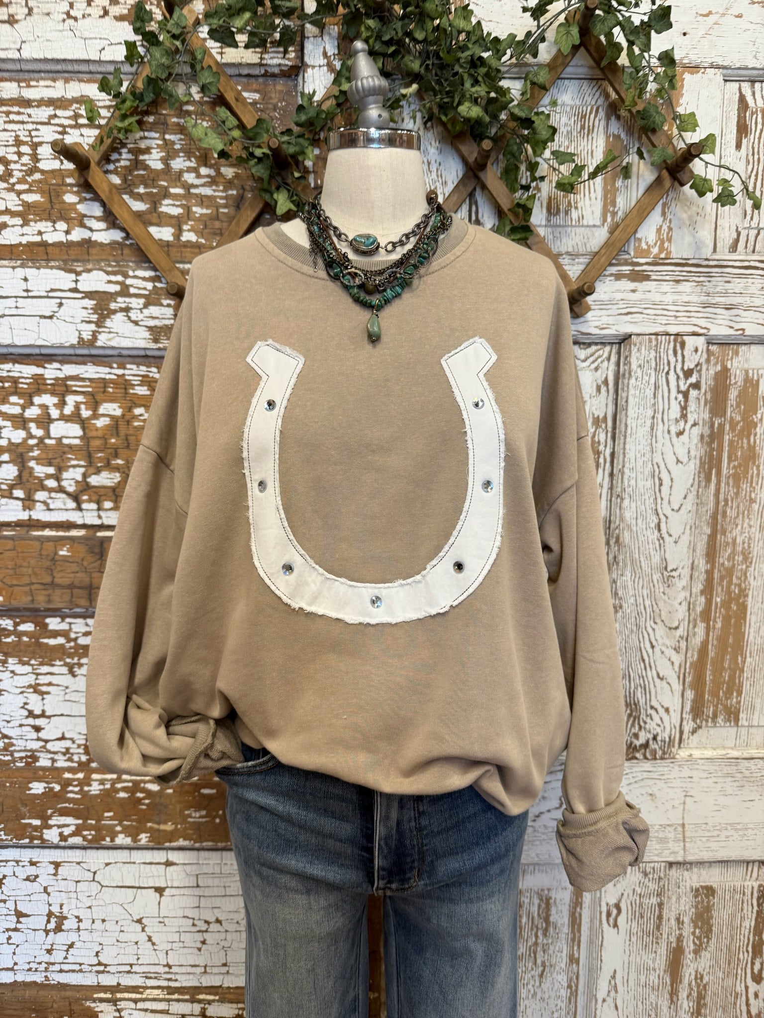 Brown sweatshirt with horseshoe design on a mannequin against a rustic wooden background