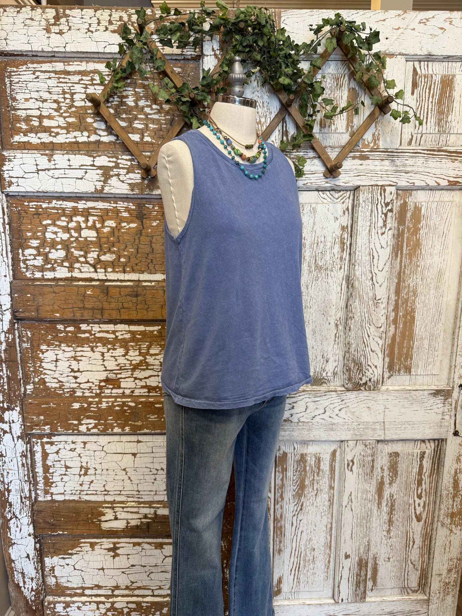 Mannequin wearing a blue sleeveless top and  jeans against a rustic wooden wall