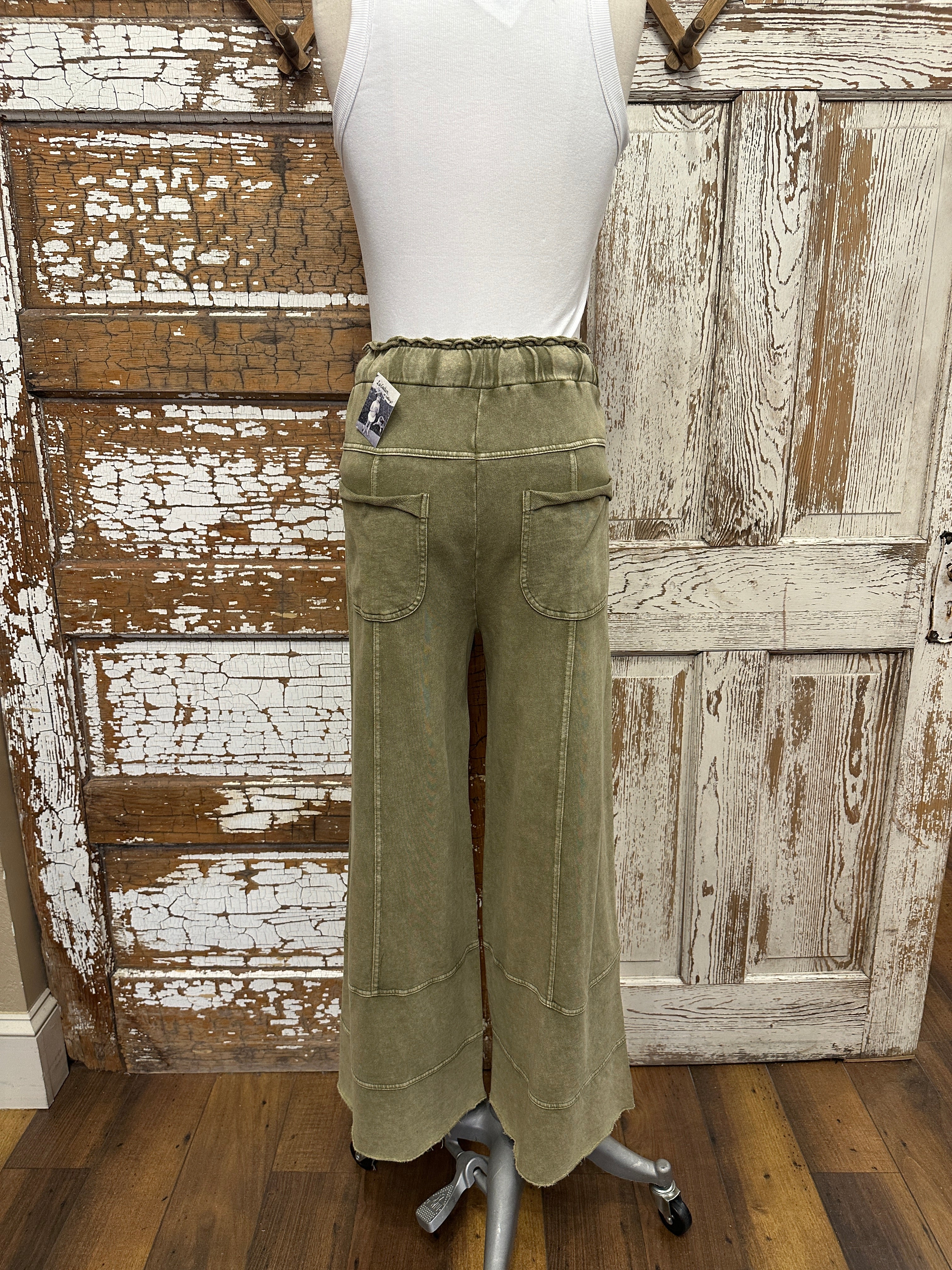 Mannequin wearing leisurewear pants against a rustic wooden wall.