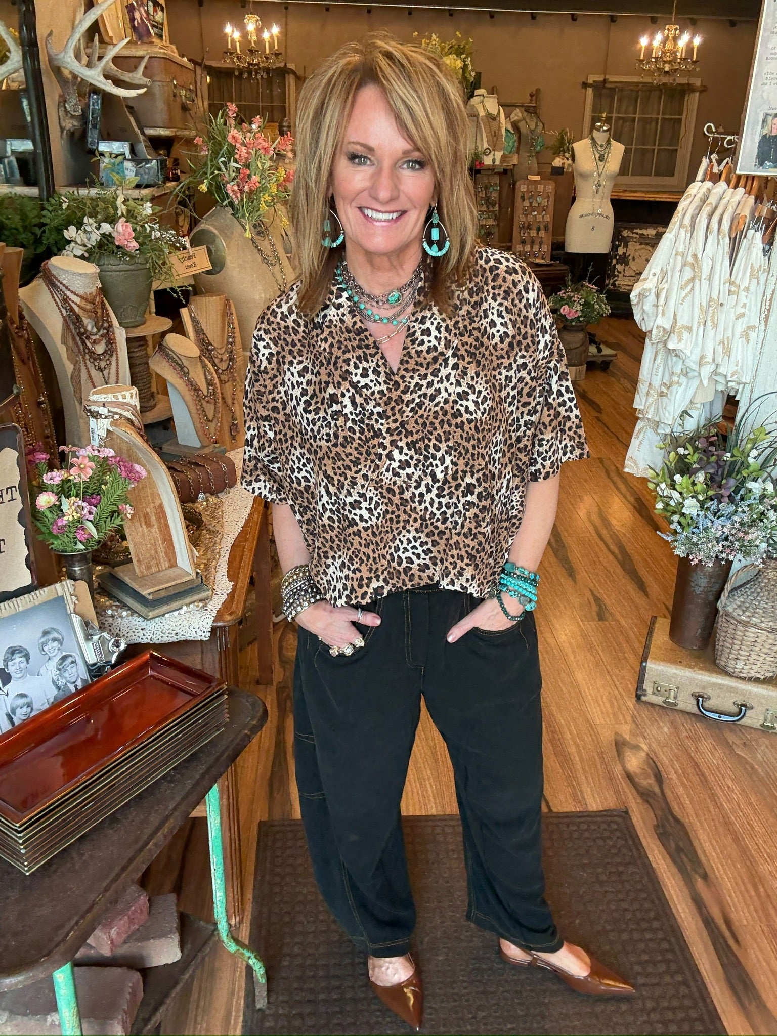 Lu wearing a leopard print collared top with handmade turquoise jewelry and barrel jeans in Leavenworth, KS boutique