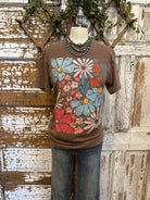 Mannequin wearing a brown graphic tee shirt with floral design and blue jeans against a rustic wooden wall.