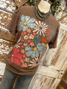 Mannequin wearing a brown graphic tee shirt with floral design and blue jeans against a rustic wooden wall.