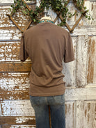 Mannequin wearing a brown graphic tee shirt with floral design and blue jeans against a rustic wooden wall.