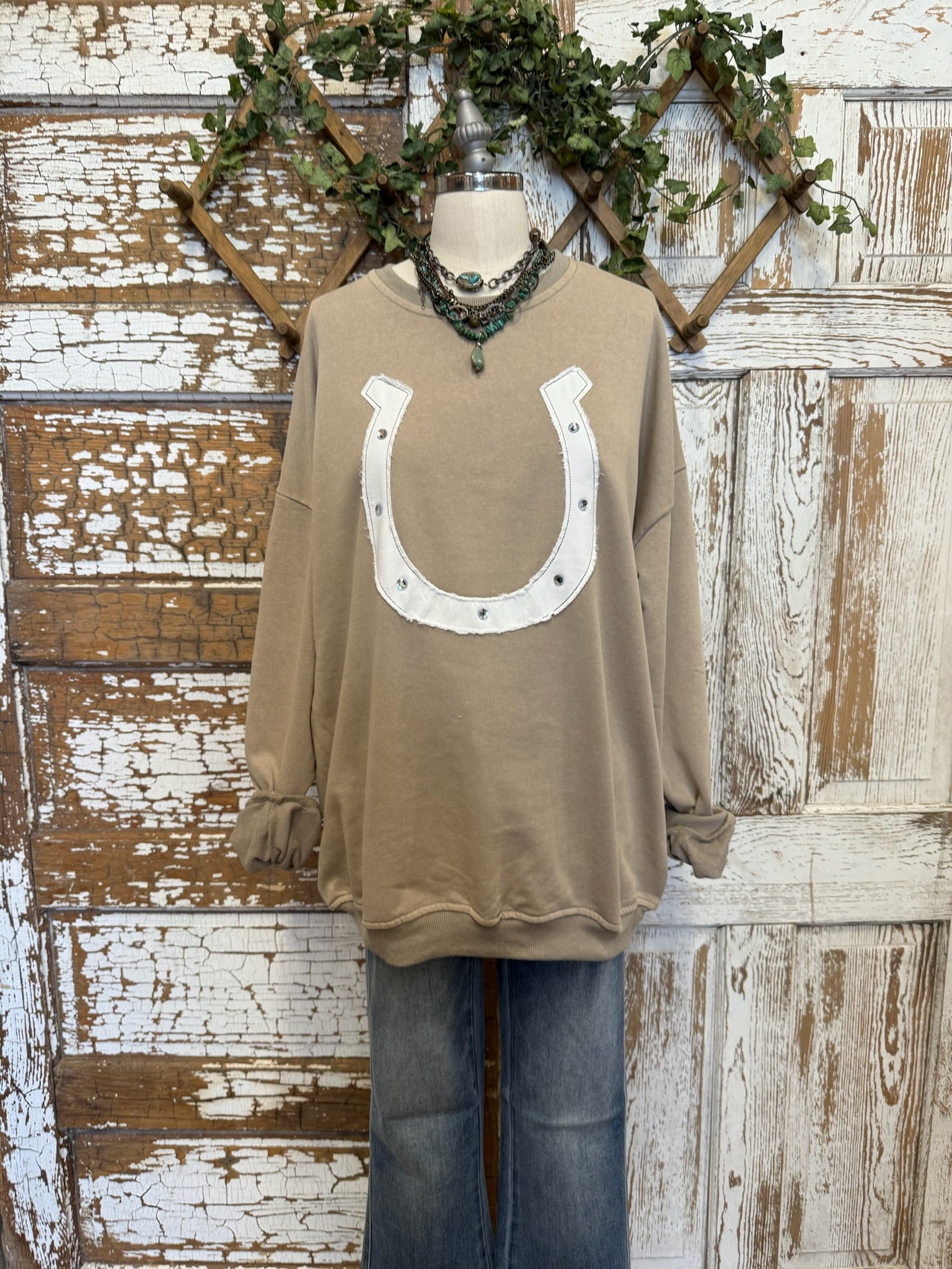 Taupe sweatshirt with a horseshoe design on a mannequin against a rustic wooden background