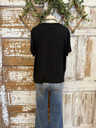 Mannequin wearing a black t-shirt and blue jeans against a rustic wooden wall with greenery.