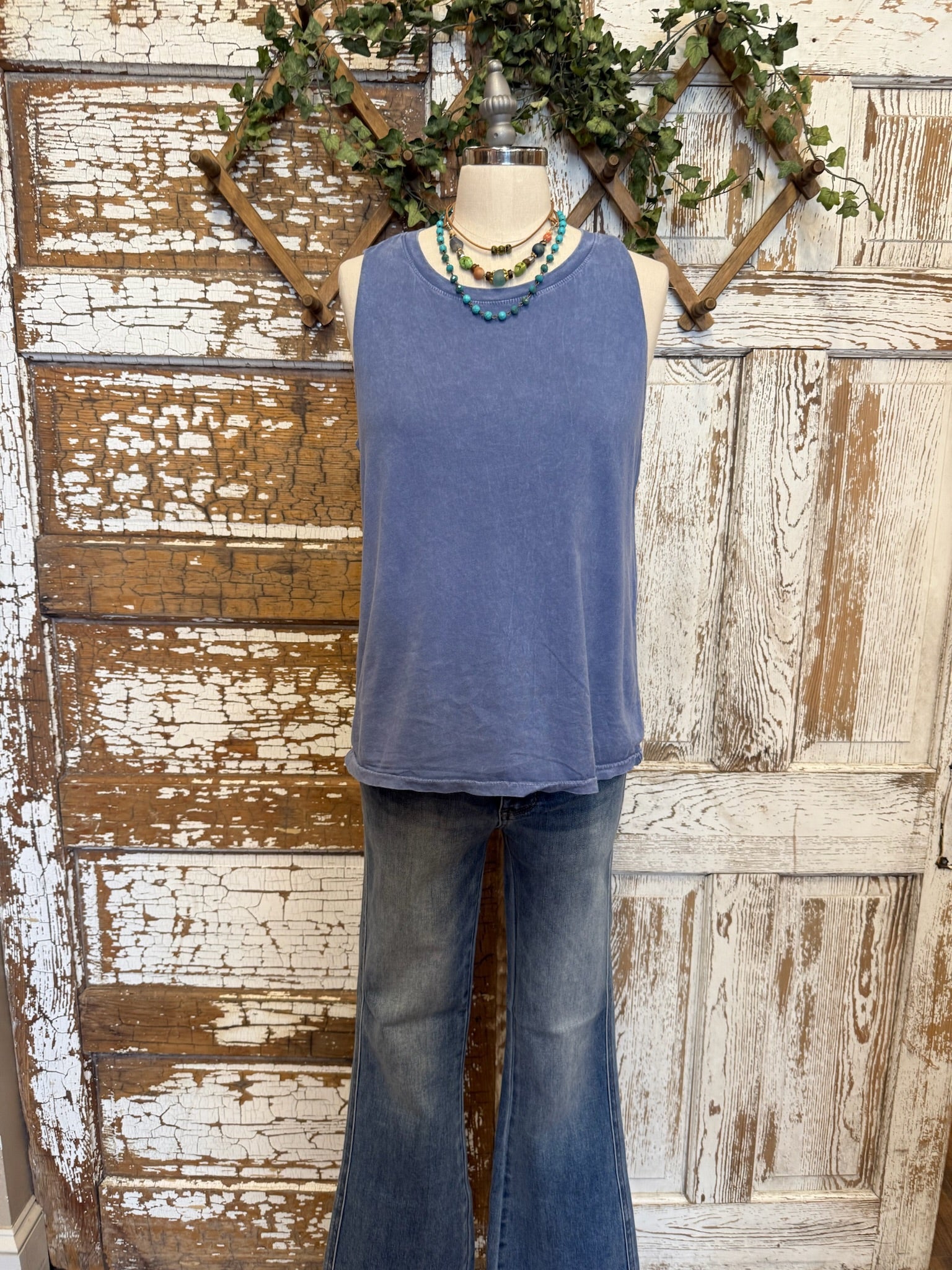 Mannequin wearing a blue sleeveless top and jeans against a rustic wooden background