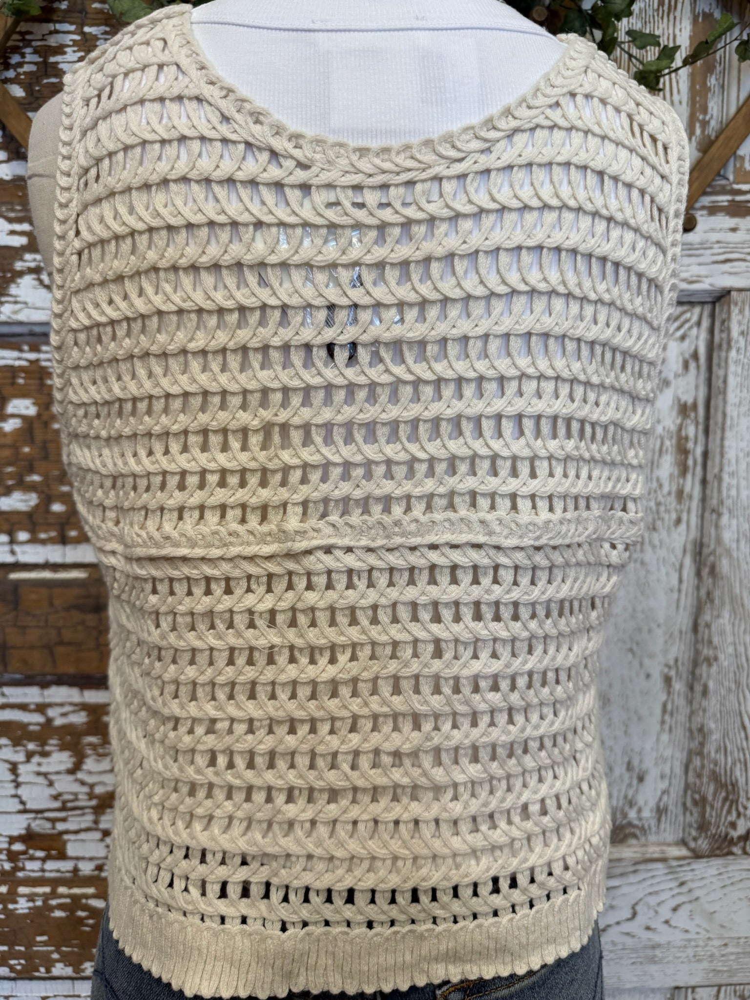 Beige knitted tank top on a mannequin against a wooden background