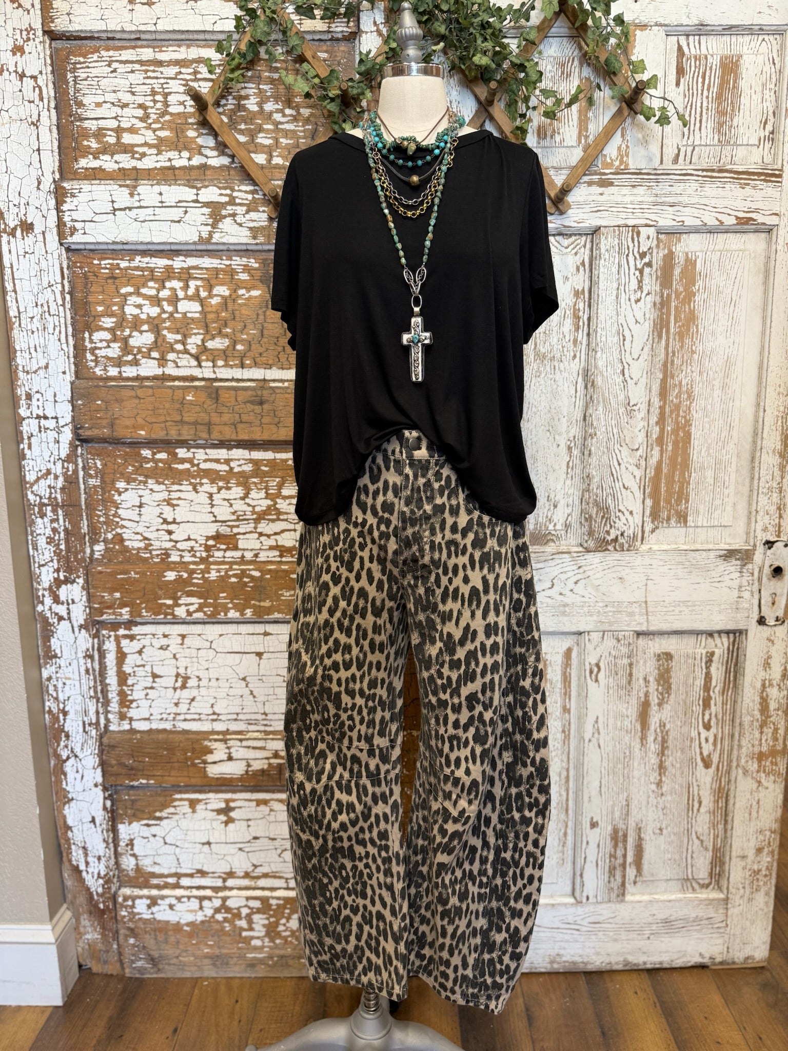 Mannequin wearing a black top and leopard print barrel pants against a rustic wooden door background