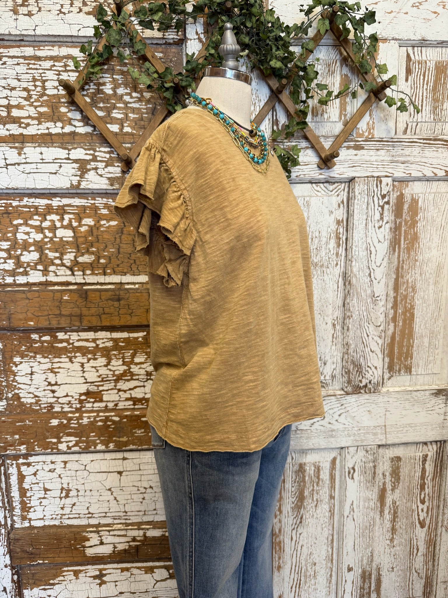 Mannequin wearing a toffee brown shirt and jean pants against a rustic wooden wall.