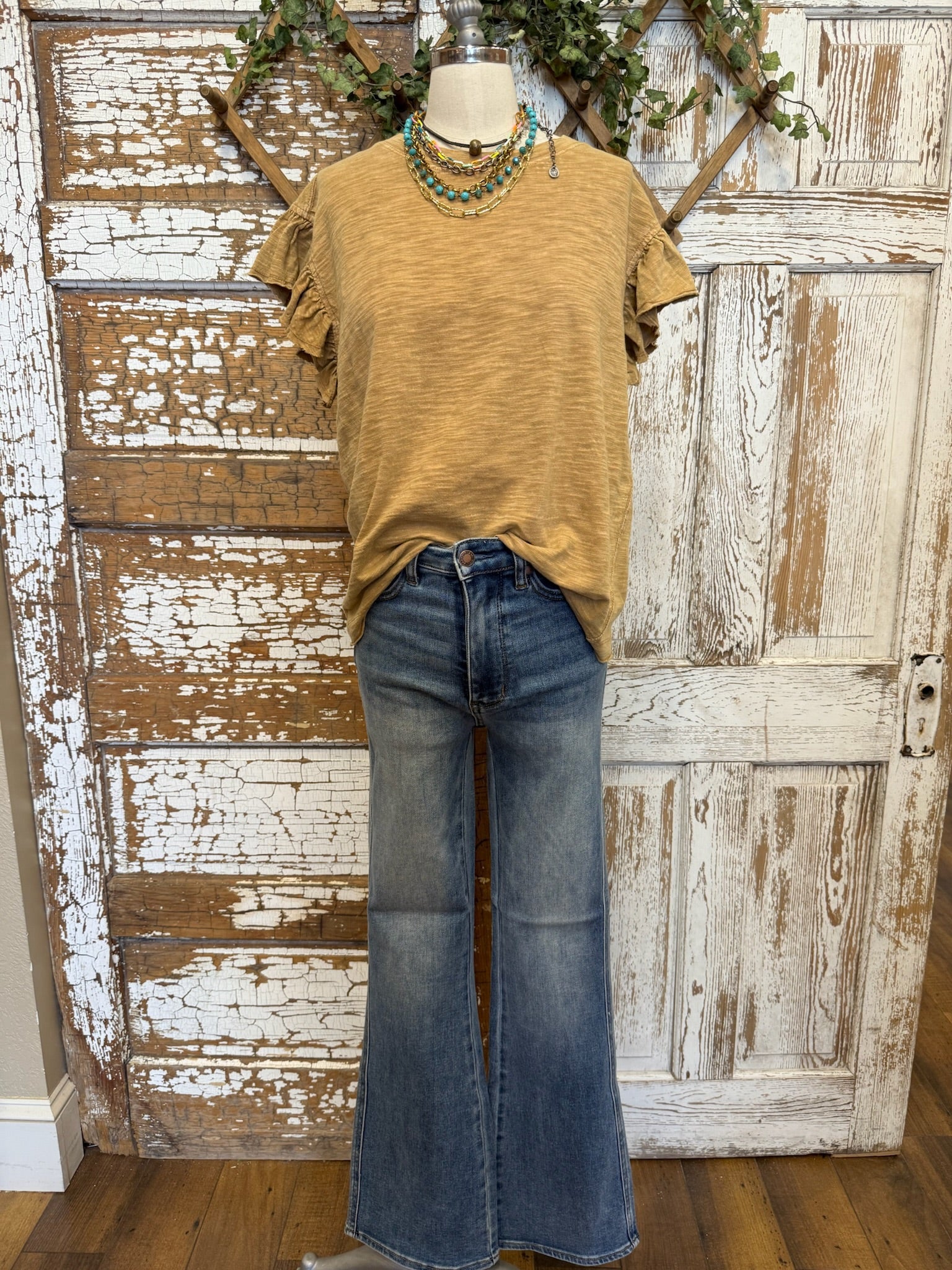 Mannequin wearing a mustard yellow top and blue jeans against a rustic wooden door background