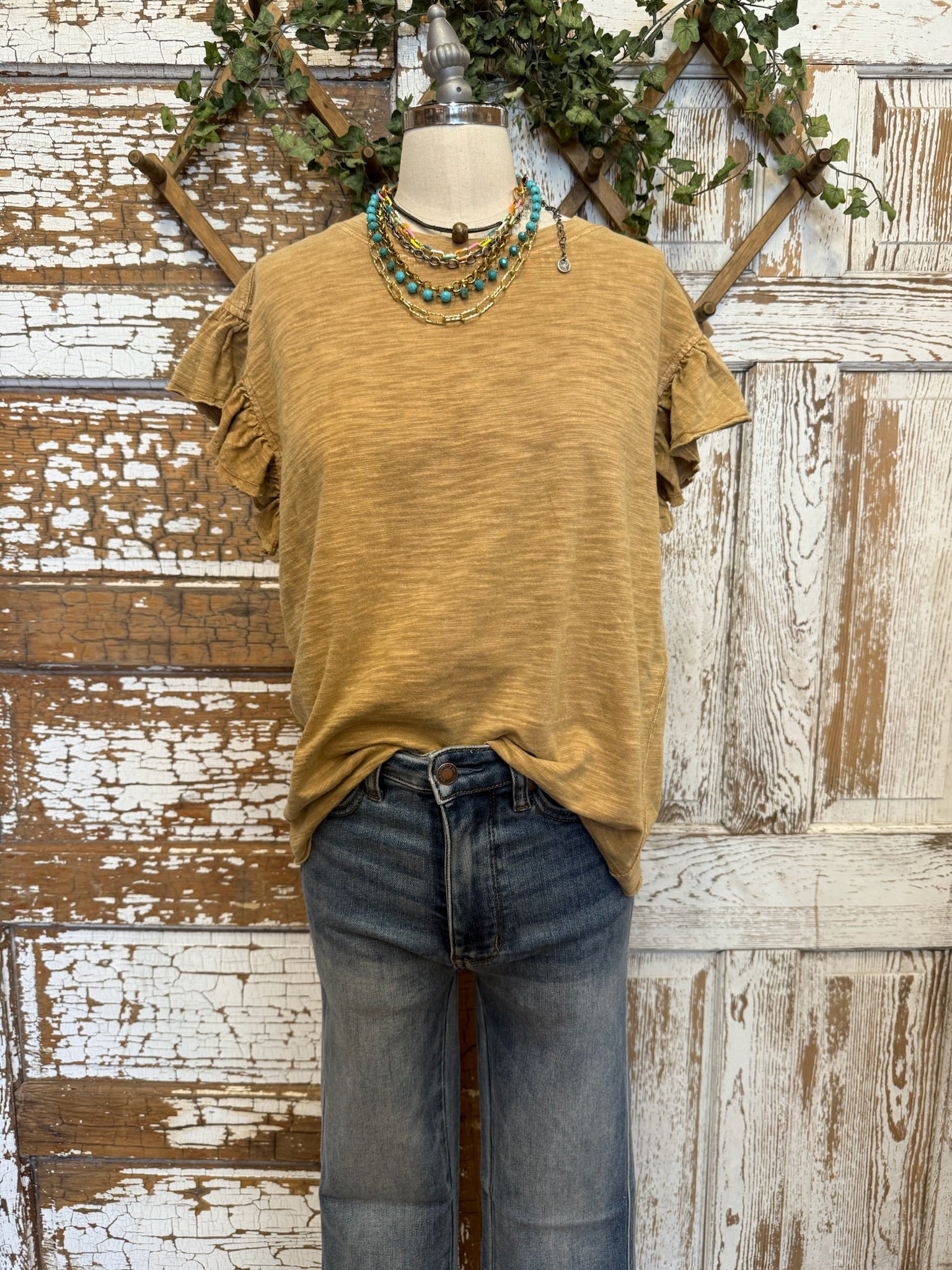 Mannequin wearing a toffee brown shirt and jean pants with layered handmade jewelry against an artistic handmade background