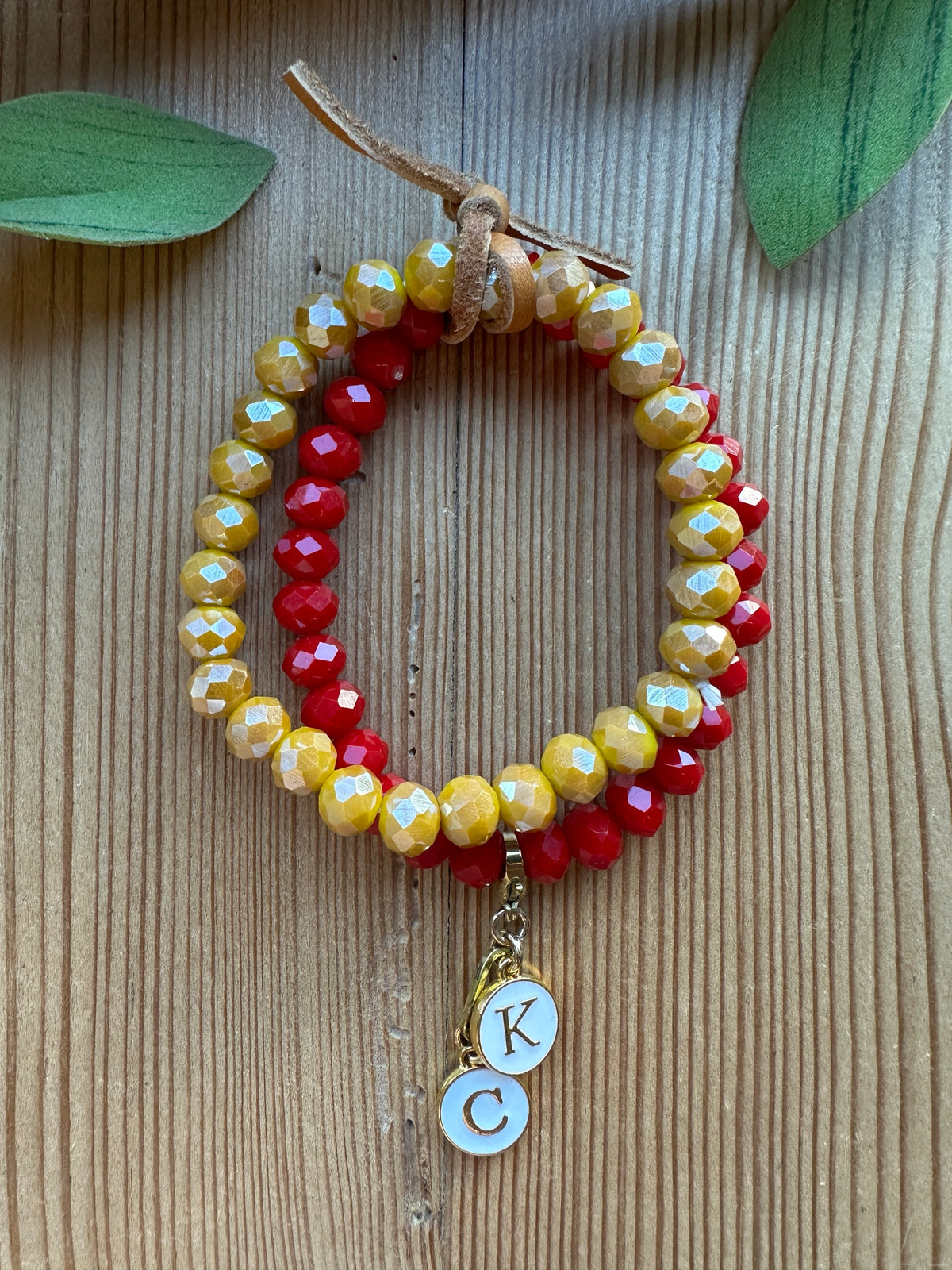 Stack of two faceted crystal stretch bracelets in golden yellow and red with gold K and C initial charms and leather tie