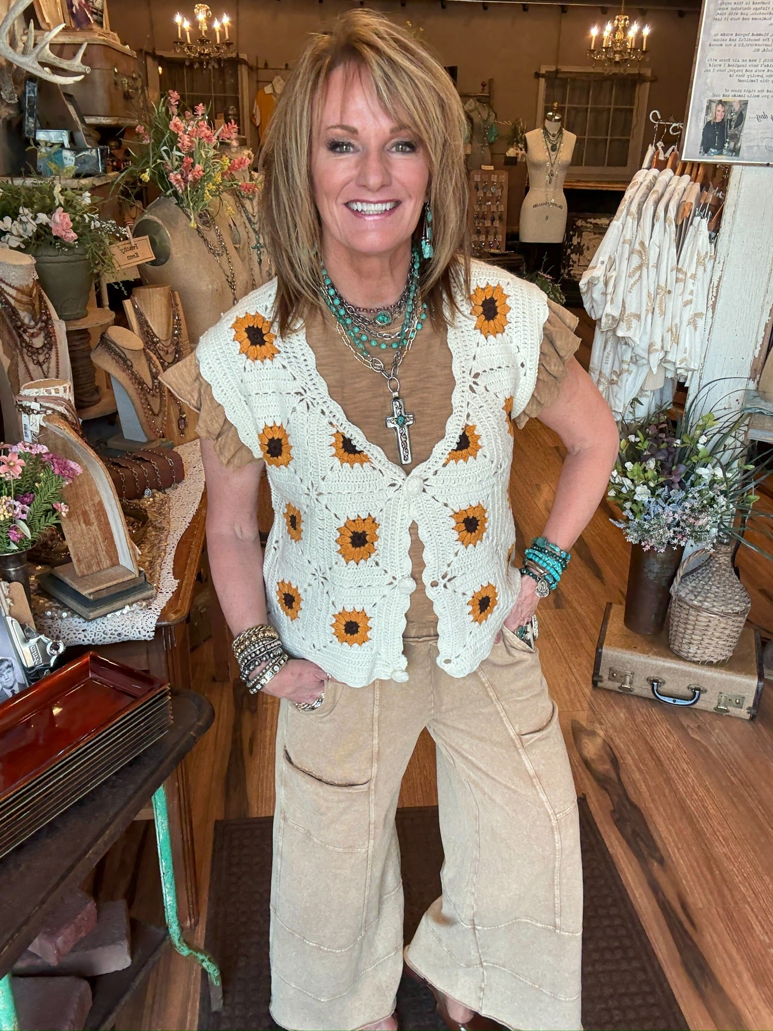 Lu wearing a sunflower-patterned  crochet vest and beige leisure pants in Lu's Leavenworth, KS boutique