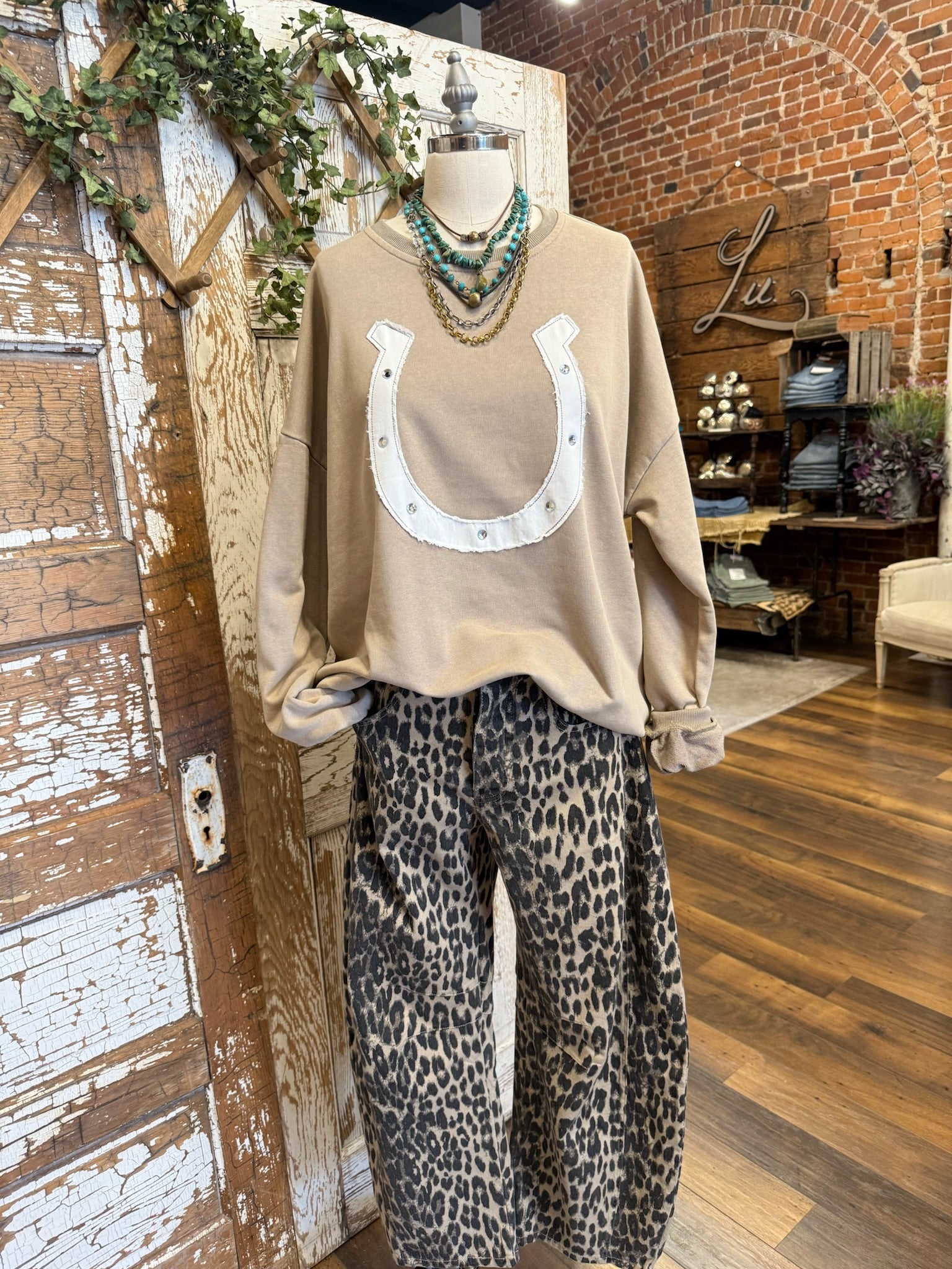 Mannequin wearing a beige sweater with a horseshoe design and leopard print barrel pants in boutique setting.
