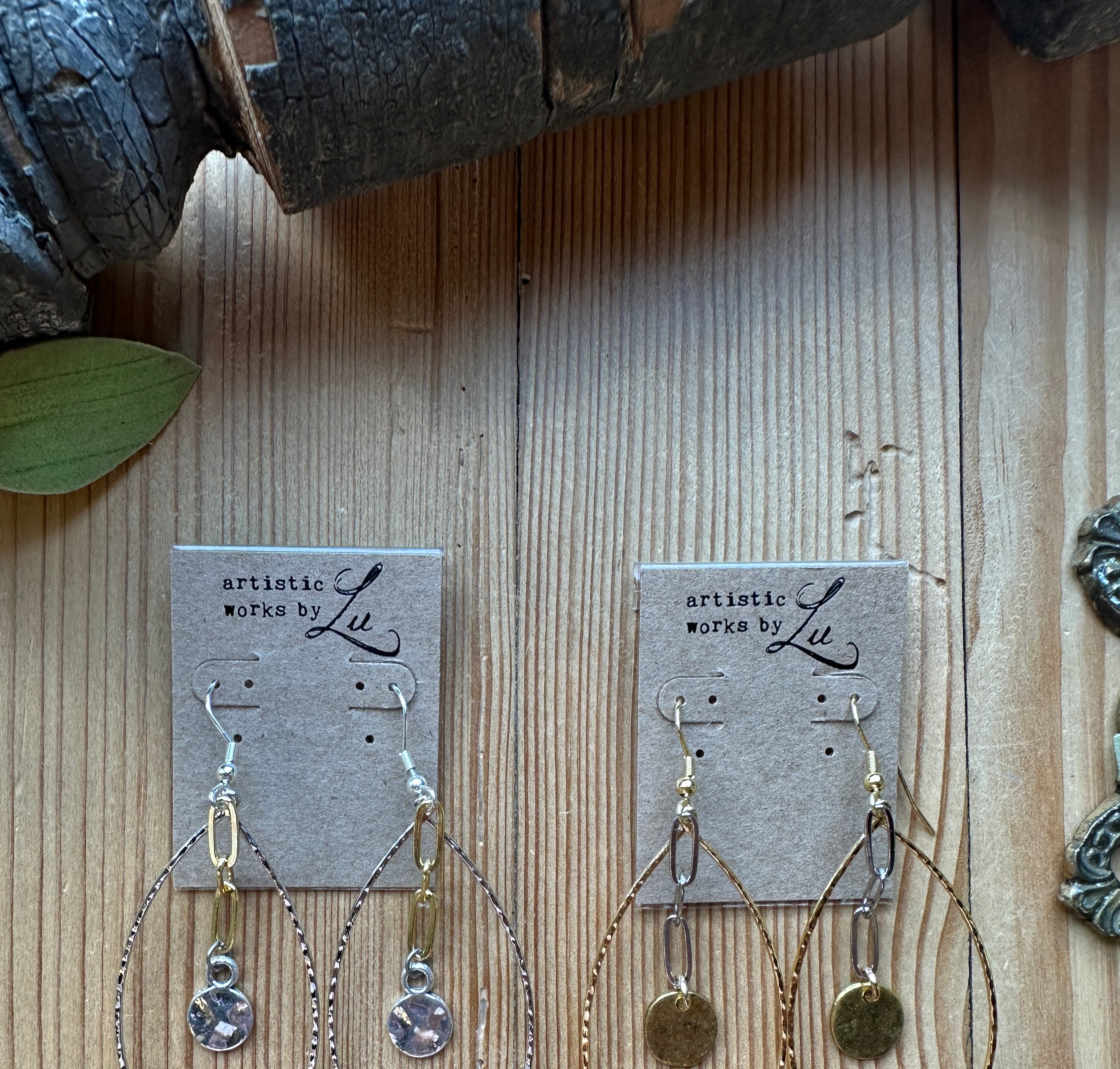 Gold hoop earrings on a wooden surface with an artistic works by lu card
