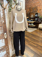 Mannequin wearing a beige sweater with a horseshoe design and black barrel pants in a store setting.