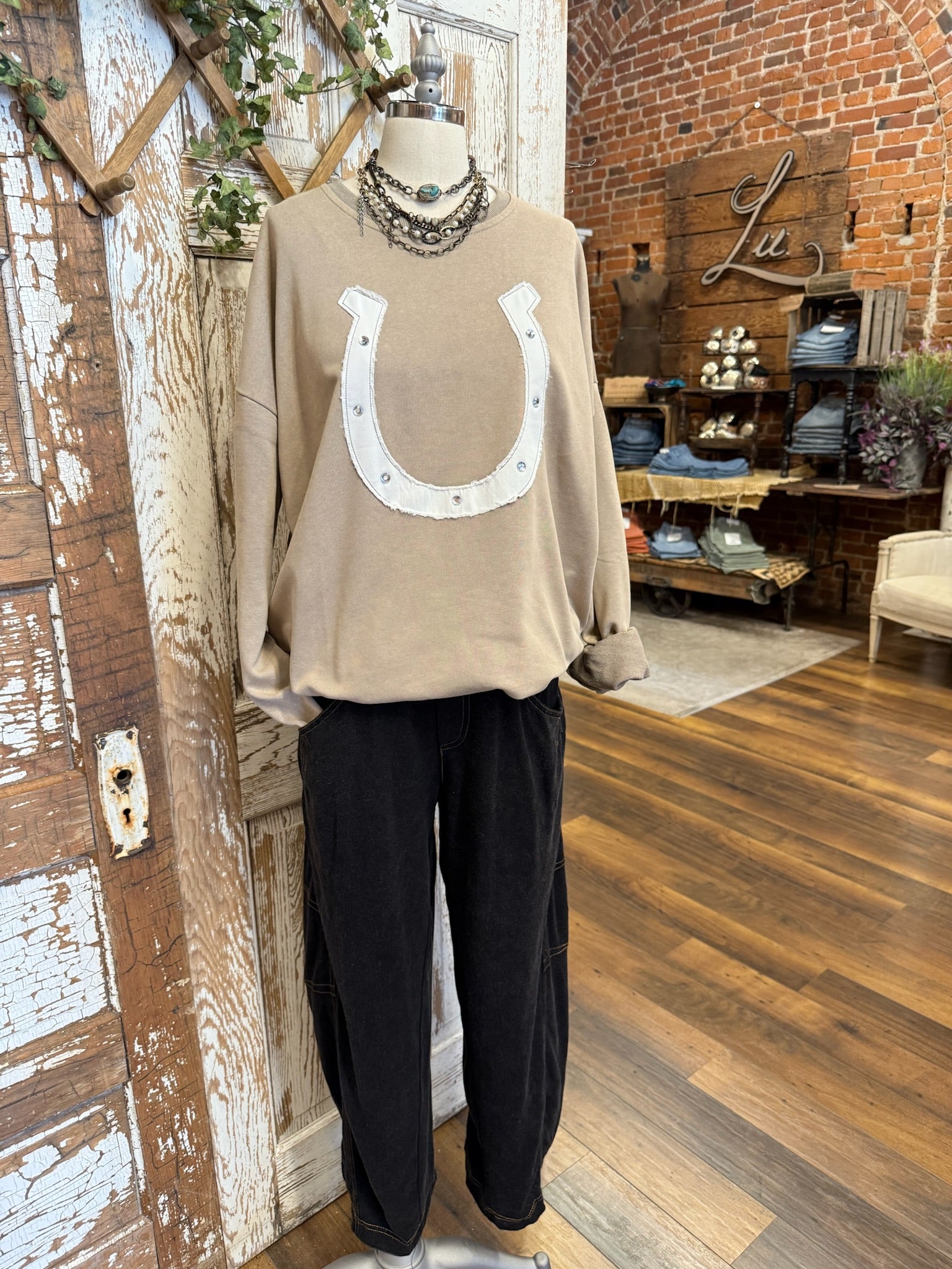 Mannequin wearing a beige sweater with a horseshoe design and black barrel pants in a store setting.