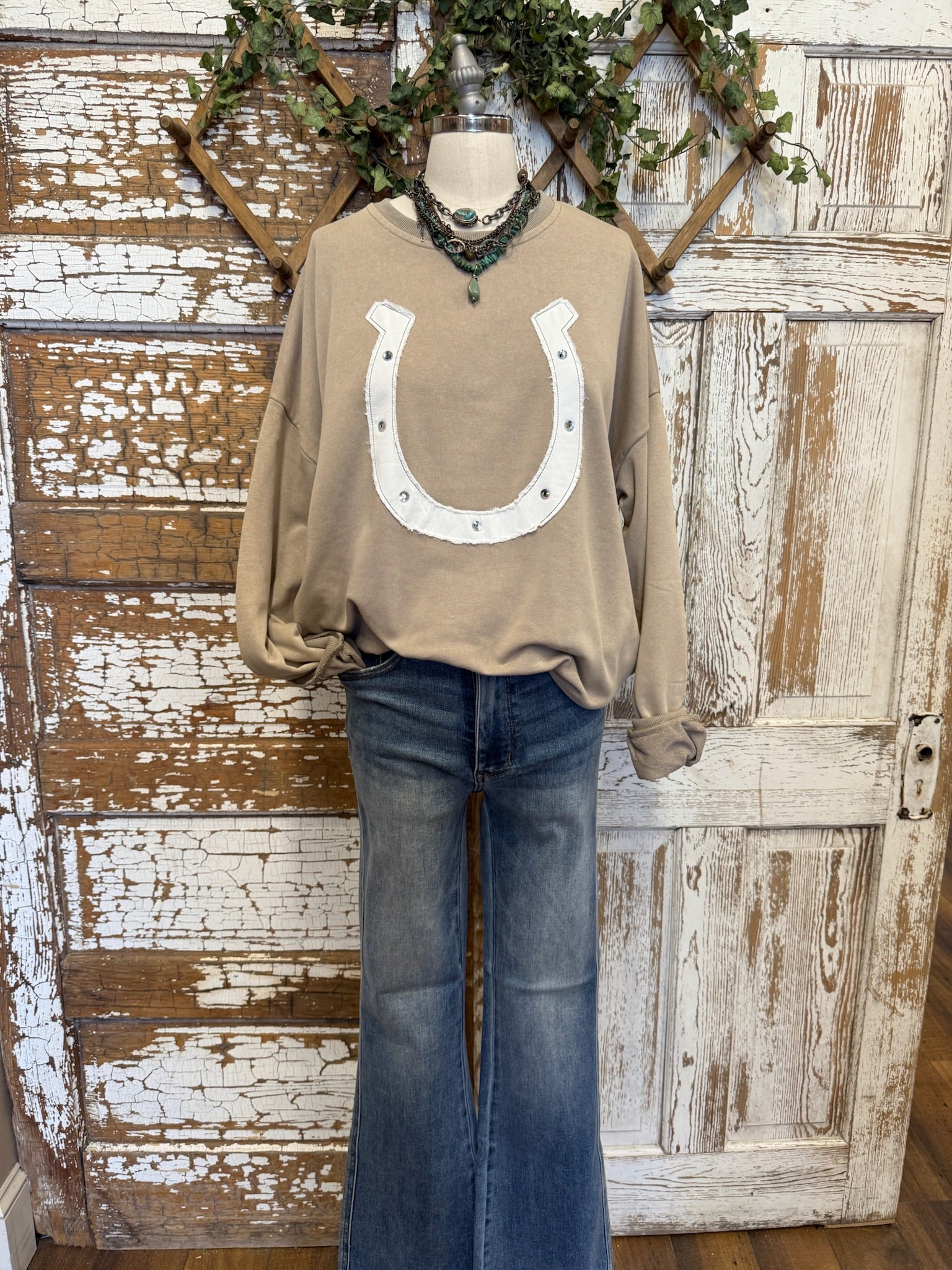 Beige long-sleeve shirt with a horseshoe design and blue jeans on a rustic wooden background