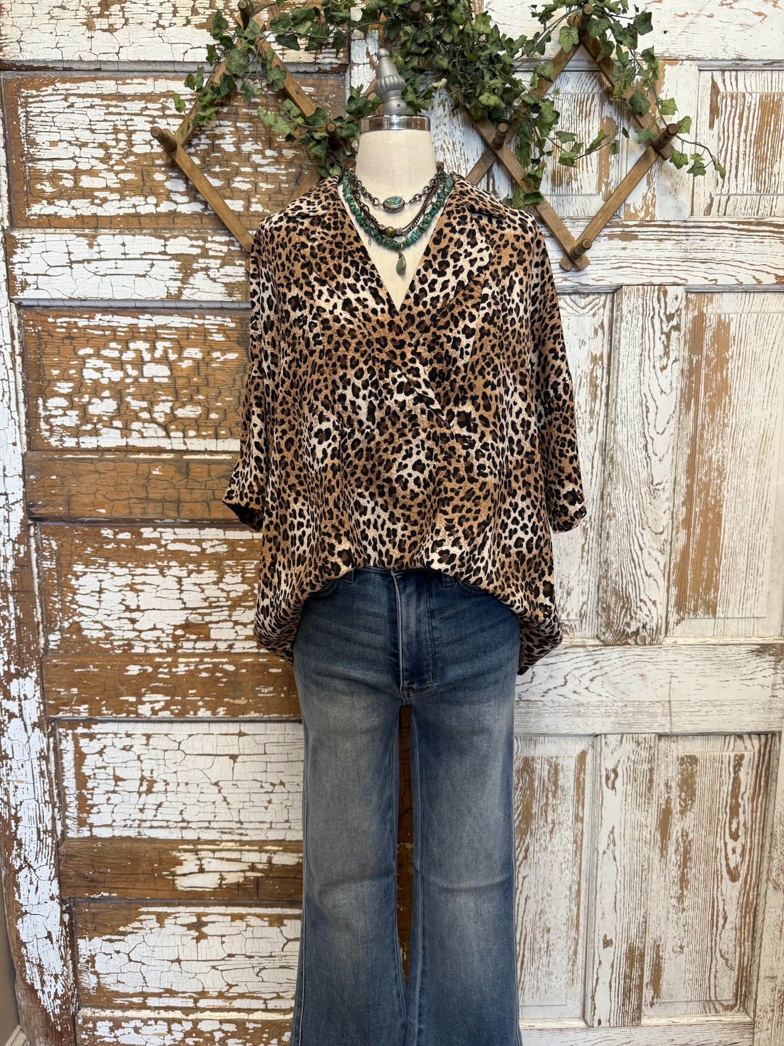Mannequin wearing a leopard print collared top with handmade turquoise jewelry and blue jeans against a rustic wooden background