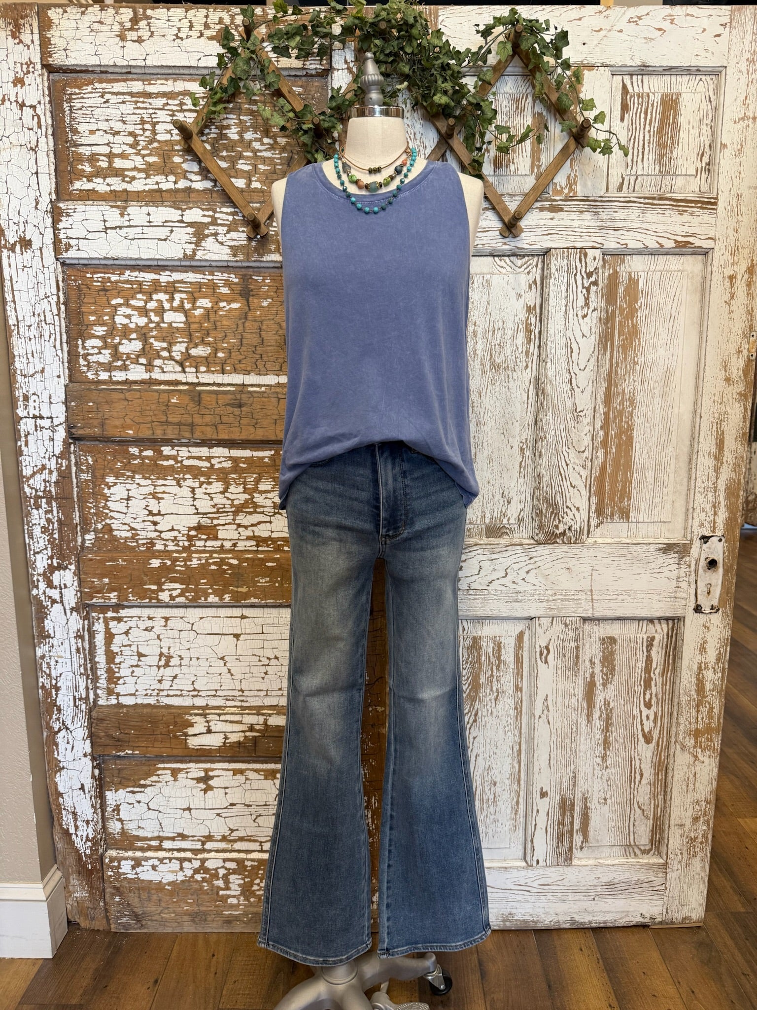 Mannequin wearing a blue sleeveless top and jeans against a rustic wooden door background