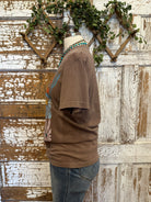 Mannequin wearing a brown graphic tee shirt with floral design and blue jeans against a rustic wooden wall.