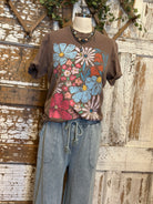 Mannequin wearing a brown graphic tee shirt with floral design and blue jeans against a rustic wooden wall.