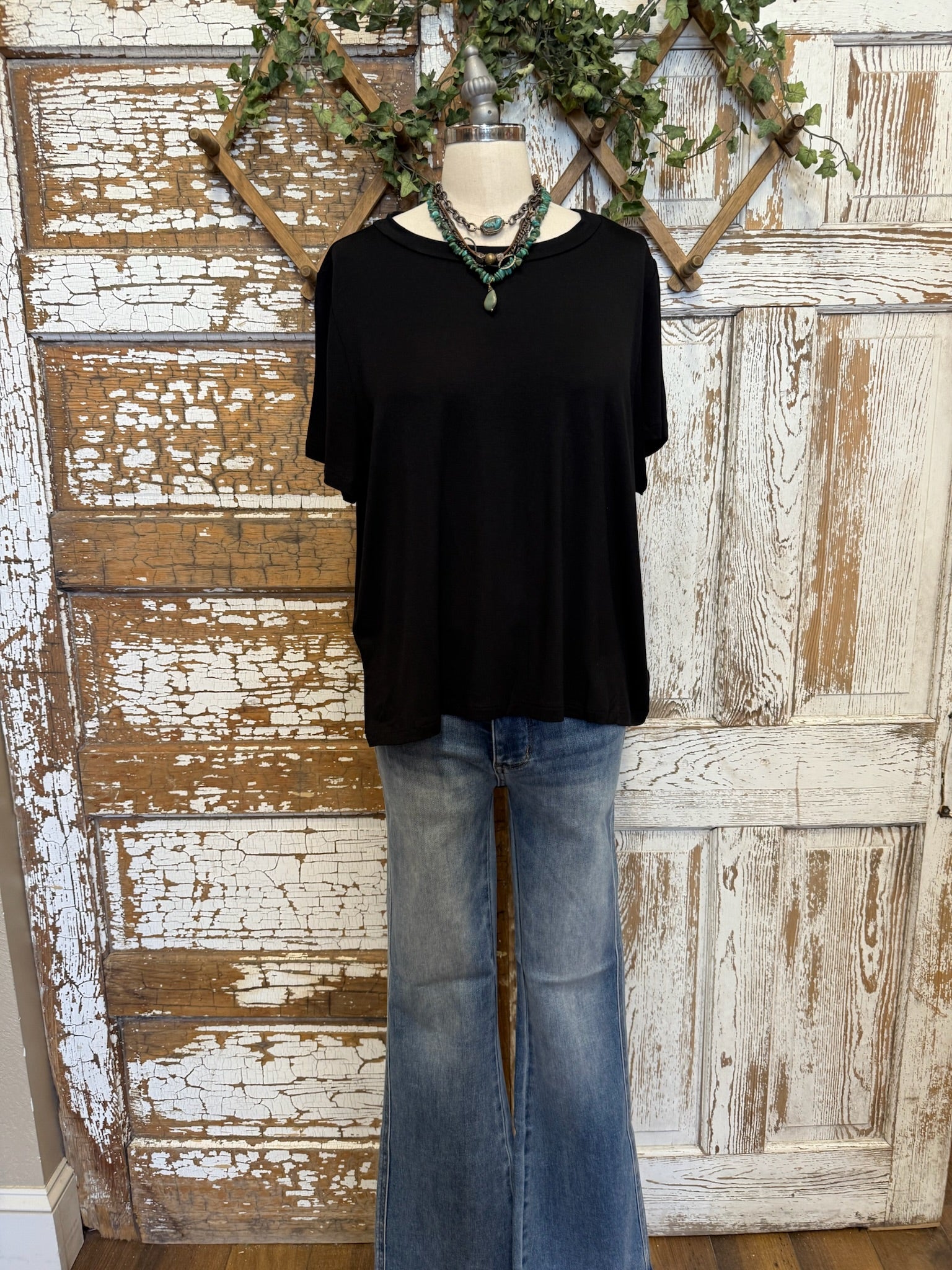 Black top, jeans and handmade jewelry worn by a mannequin against an artistic background