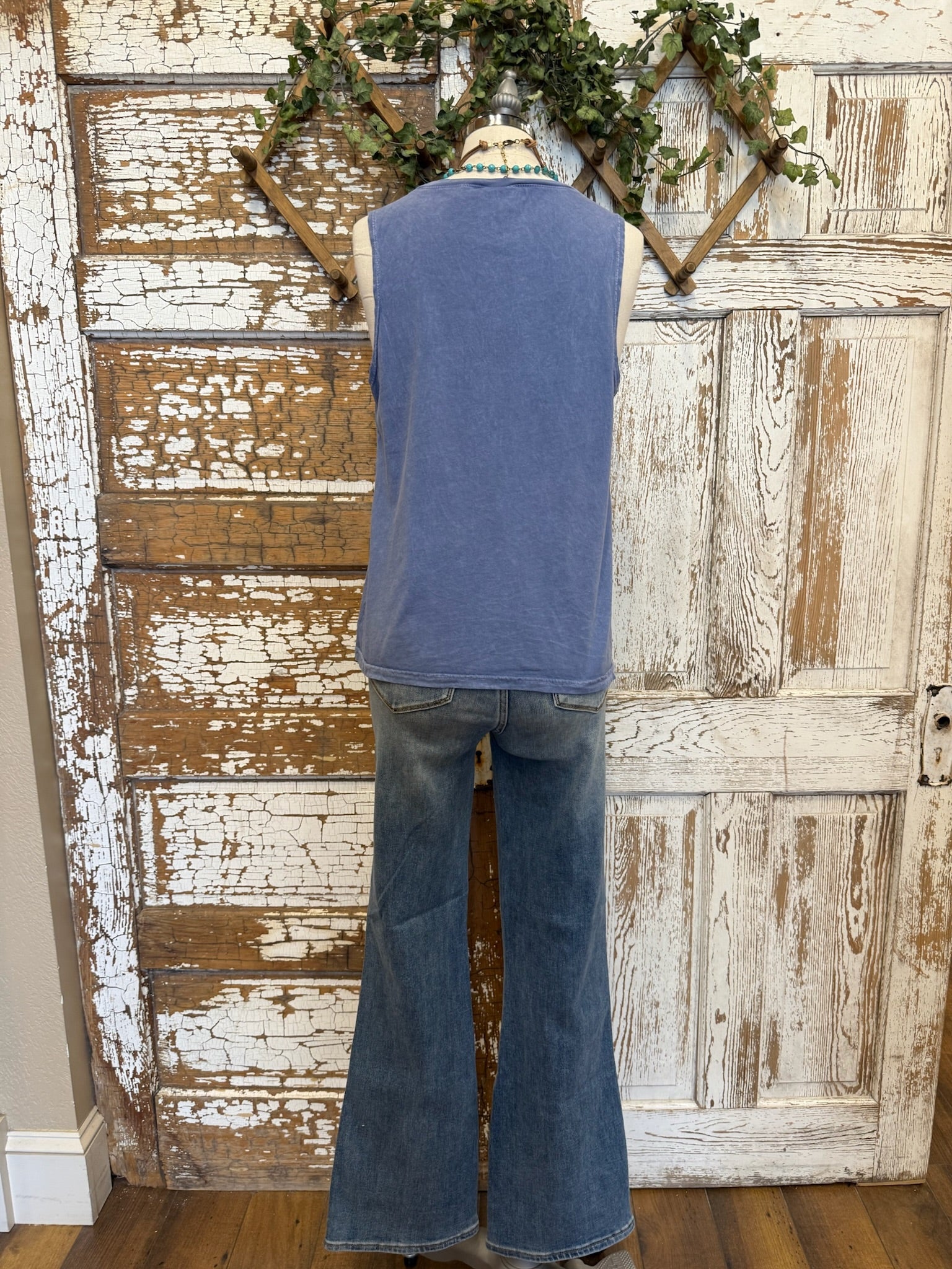 Mannequin wearing a blue sleeveless top and flared jeans against a rustic wooden door background