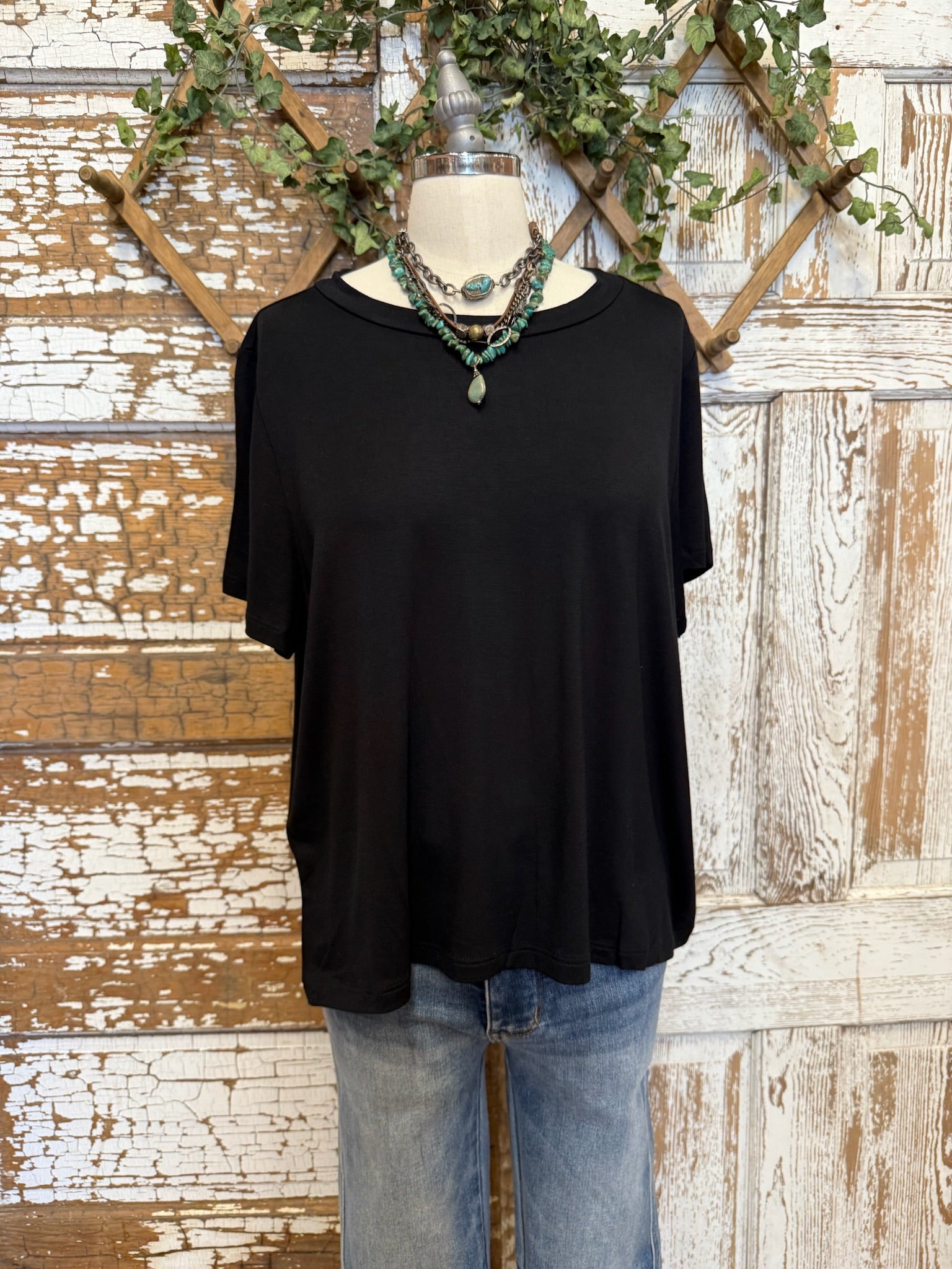 Black top and handmade jewelry worn by a mannequin against an artistic background