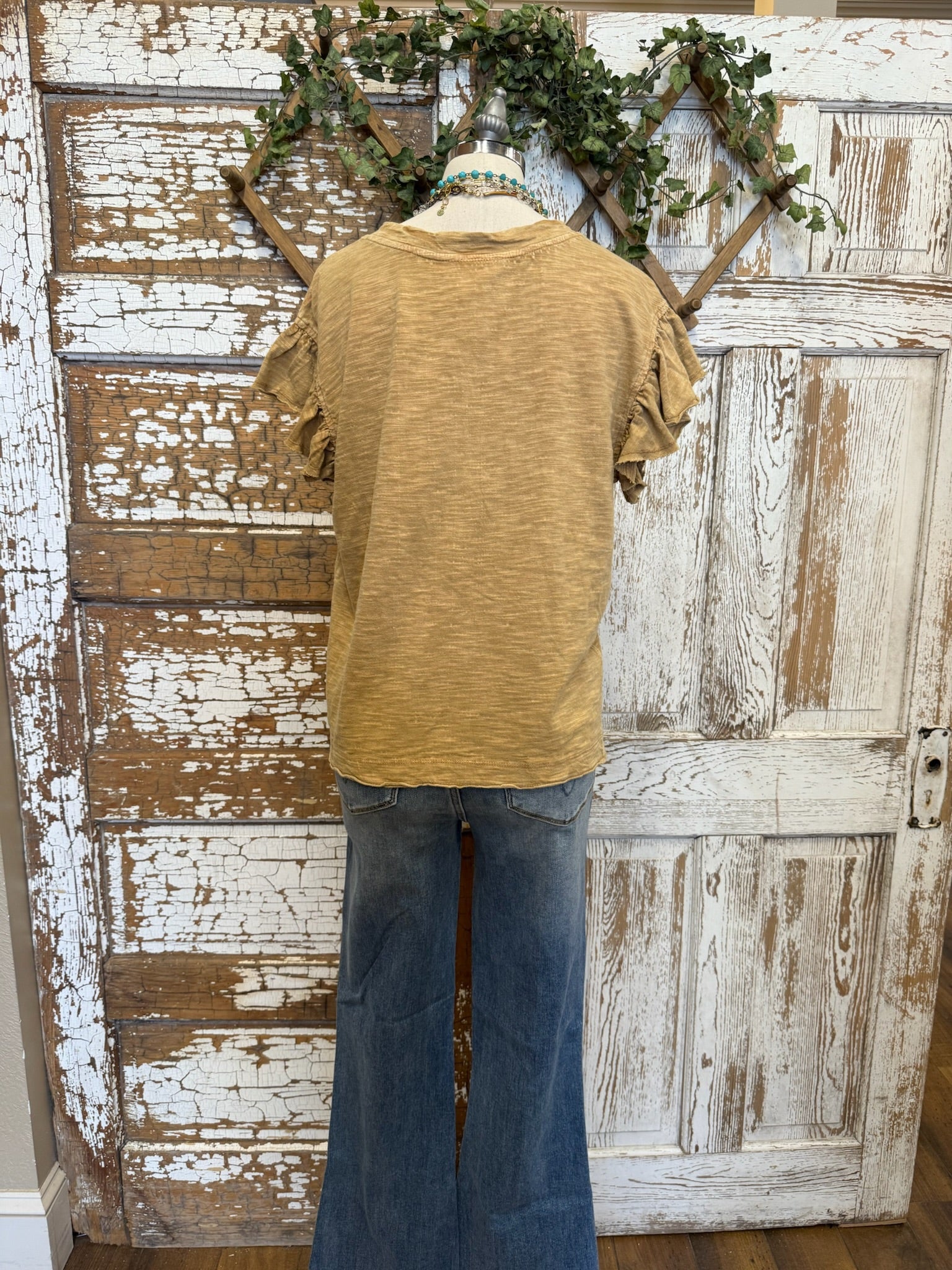 Mannequin wearing a toffee brown shirt and jean pants against a rustic wooden wall.