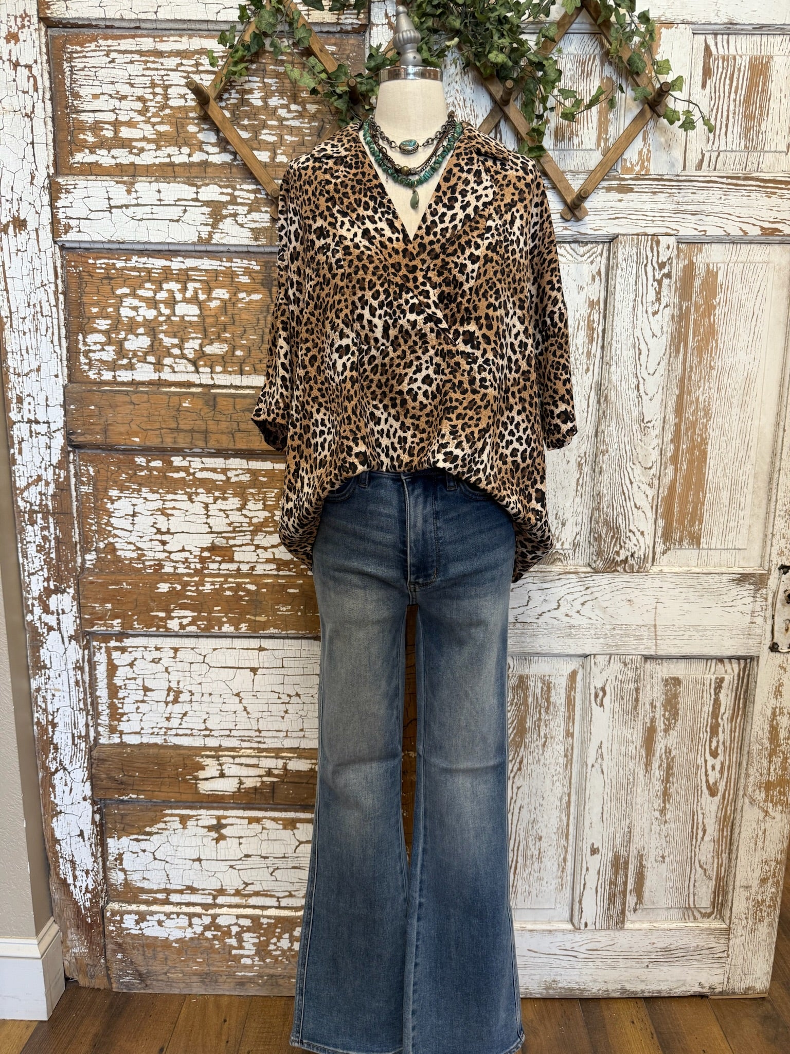 Mannequin wearing a leopard print top and blue jeans against a rustic wooden wall.
