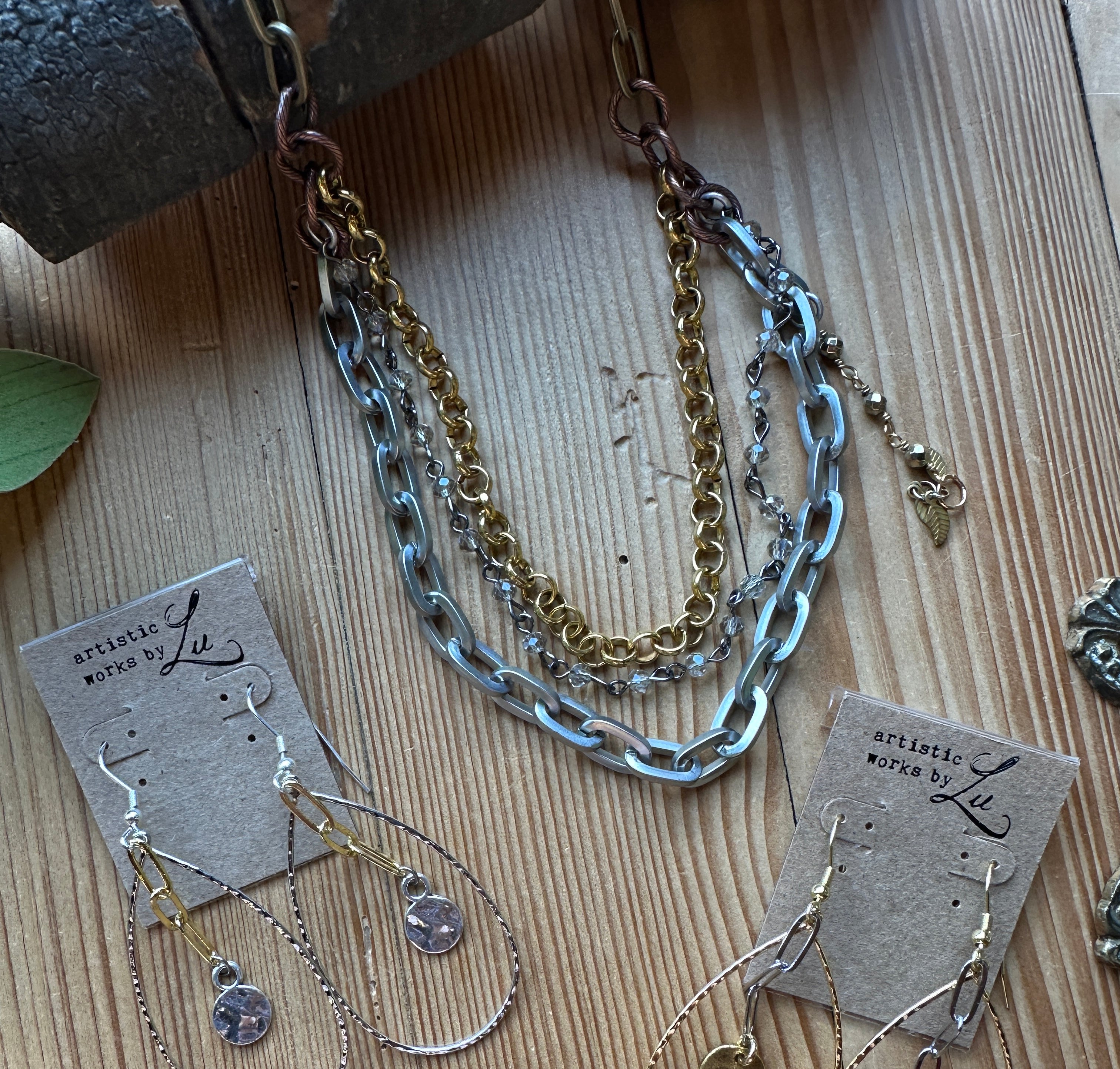 Gold and antique silver chains with delicate beads in necklace and earrings with tags on a wooden surface