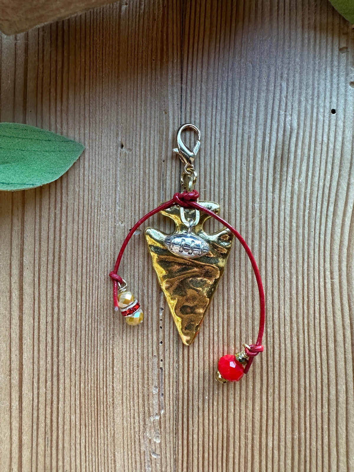 Gold arrowhead clip-on charm with silver football charm, red leather cord, and red and gold crystal bead drops