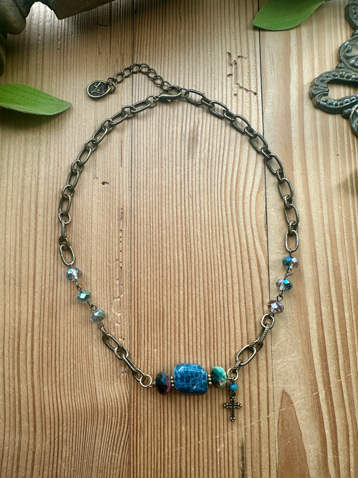 Blue Stone Cross Necklace by Artistic Works by Lu — antiqued brass chain necklace with a crackled blue stone focal bead, faceted crystal accents, and a dainty cross charm
