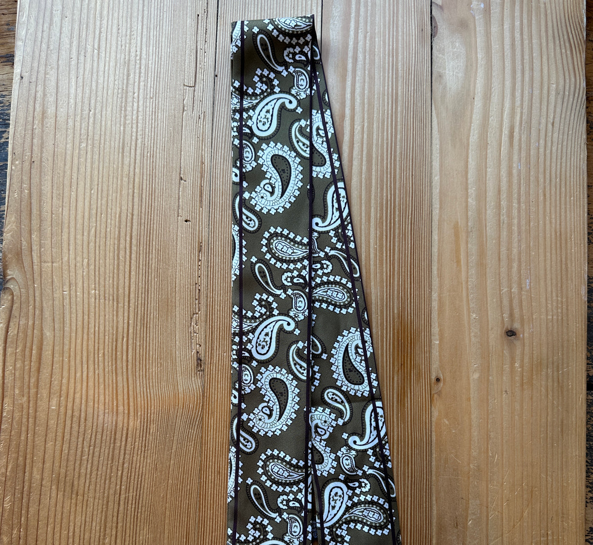 Olive paisley print silky twilly scarf laid flat on a wood surface
