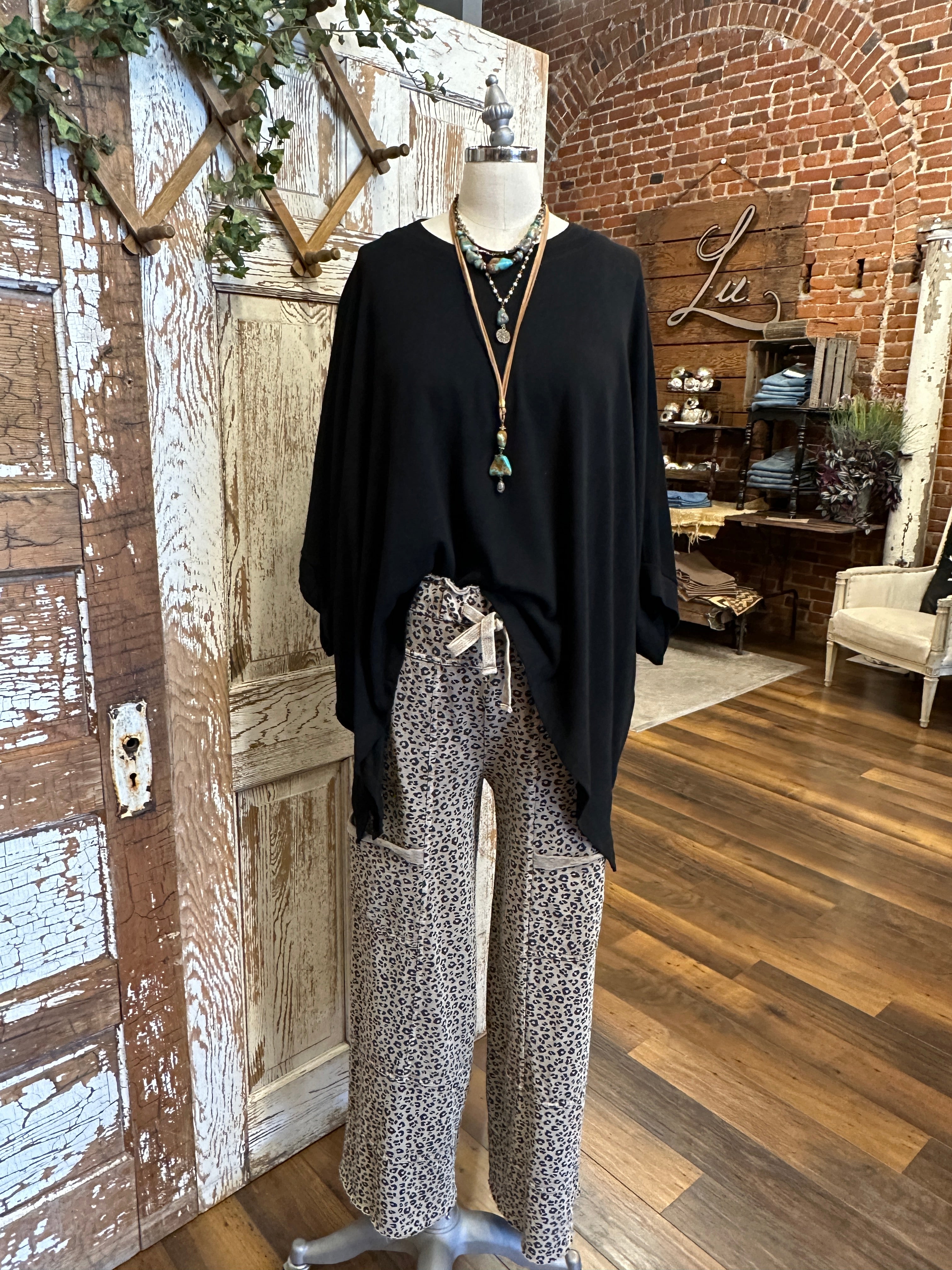 Mannequin wearing black flowy top and patterned leopard print leisurewear pants with handmade jewelry in a rustic boutique springfield, mo
