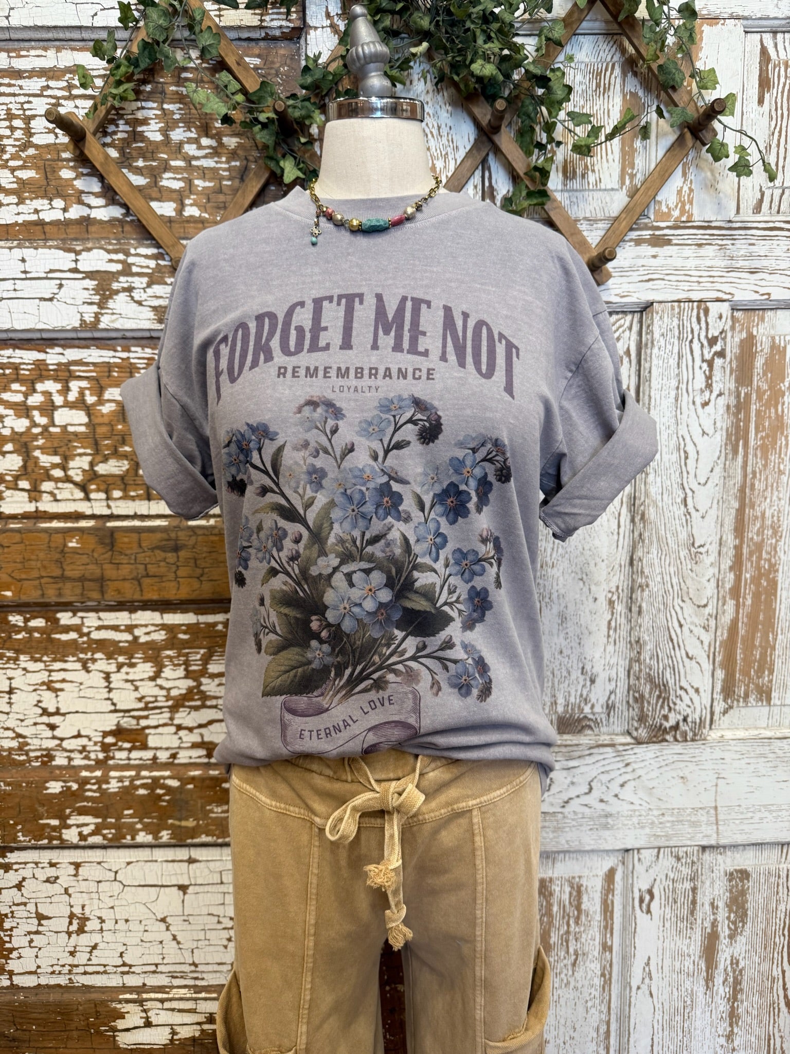 Mannequin wearing a gray t-shirt with 'Forget me not' text and beige loungewear pants against a rustic wooden door in Kansas boutique