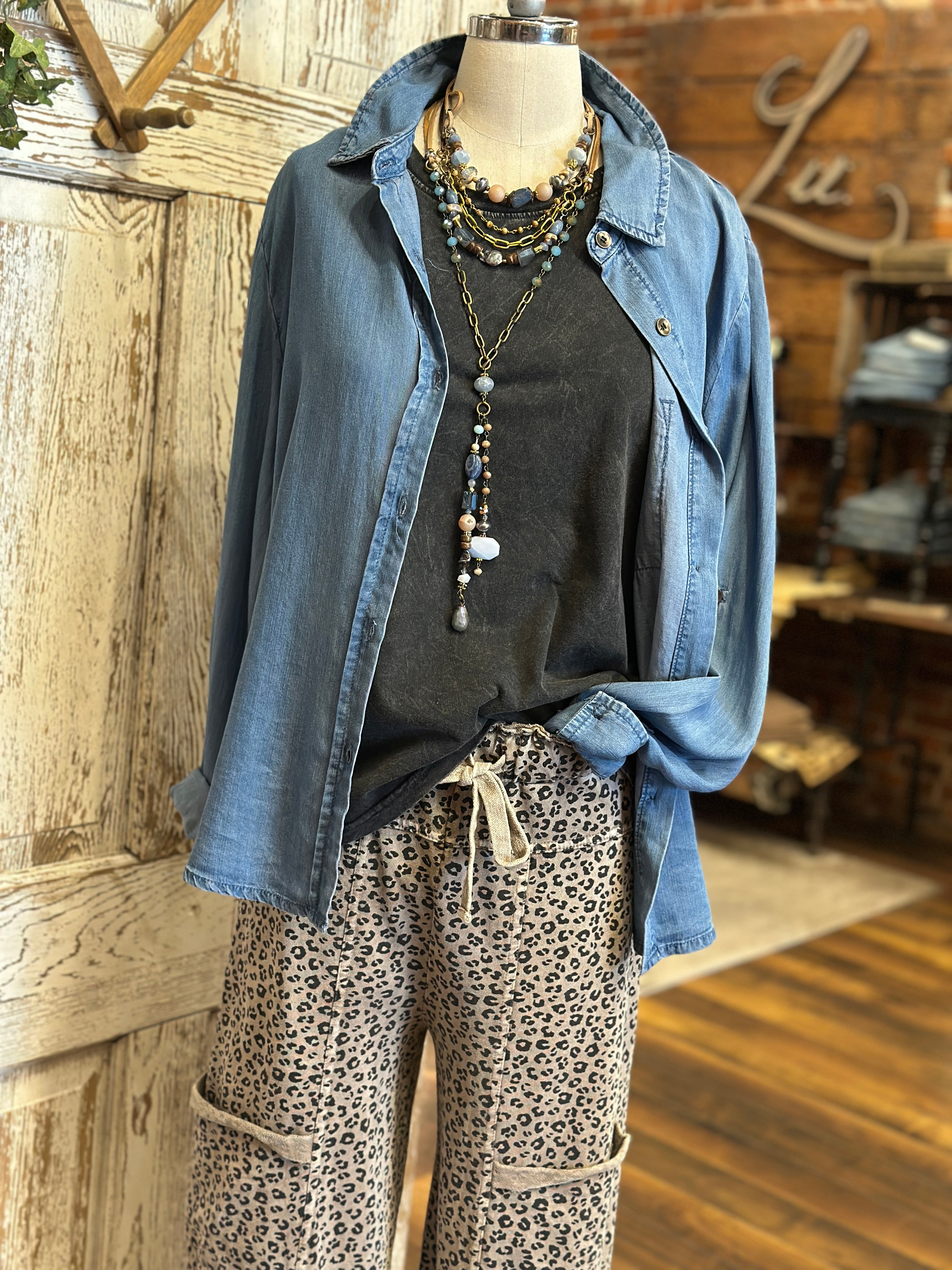 Mannequin wearing charcoal tank, denim shirt and patterned leopard print pants against a rustic boutique springfield, mo