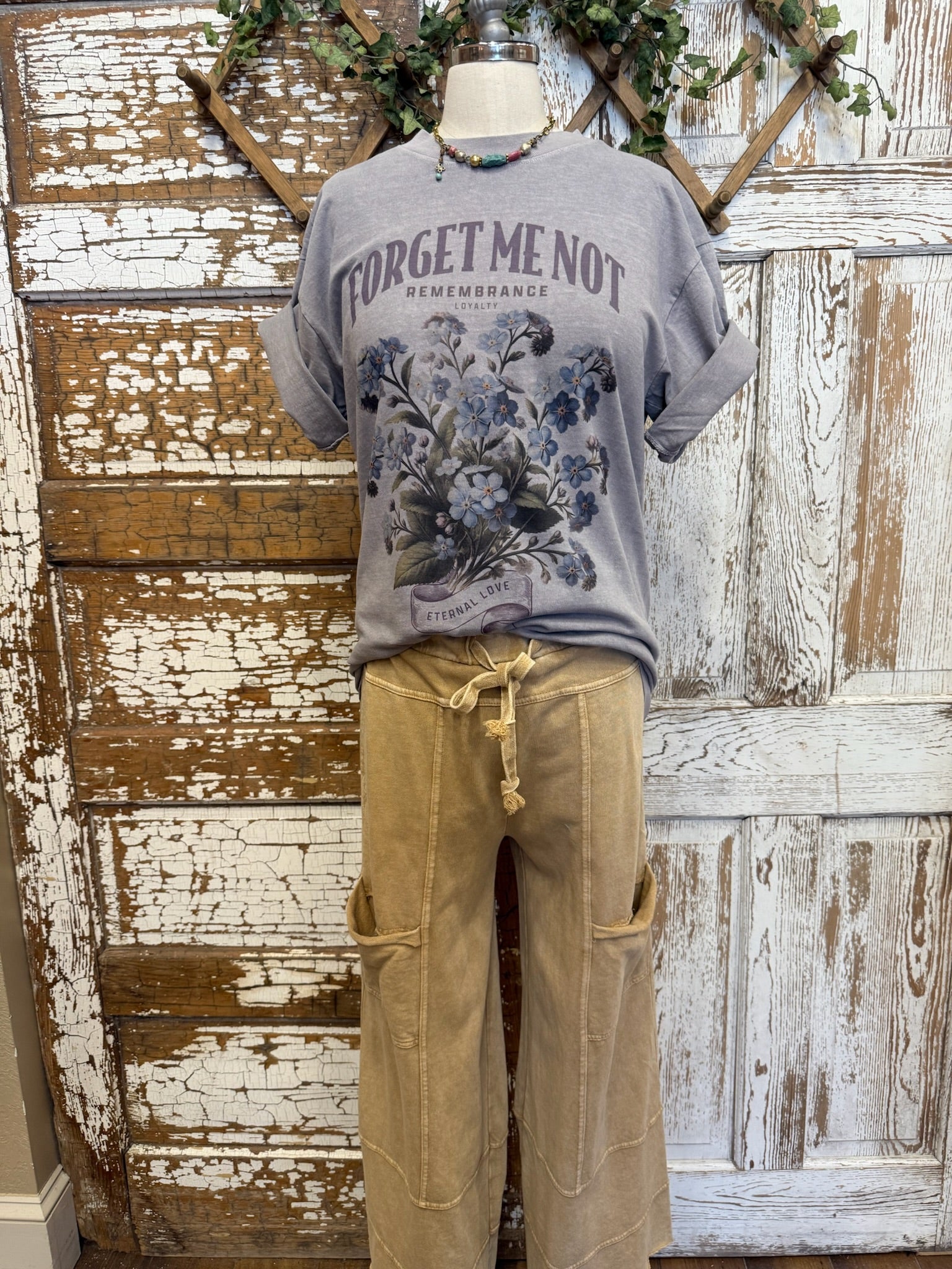 Mannequin wearing a gray t-shirt with 'Forget me not' text and beige loungewear pants against a rustic wooden door in Kansas boutique