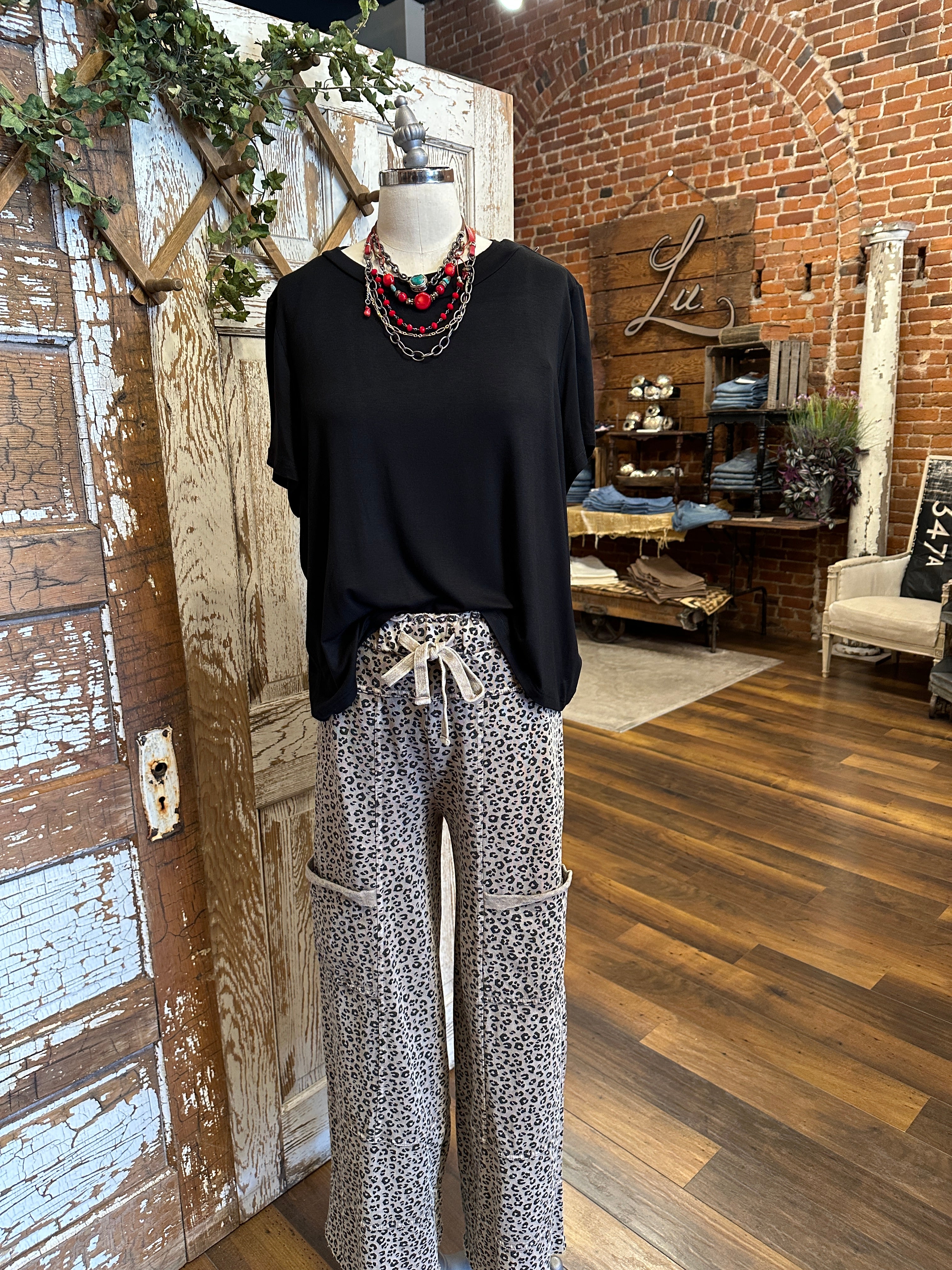 Mannequin wearing black flowy top and patterned leopard print leisurewear pants with handmade jewelry in a rustic boutique springfield, mo