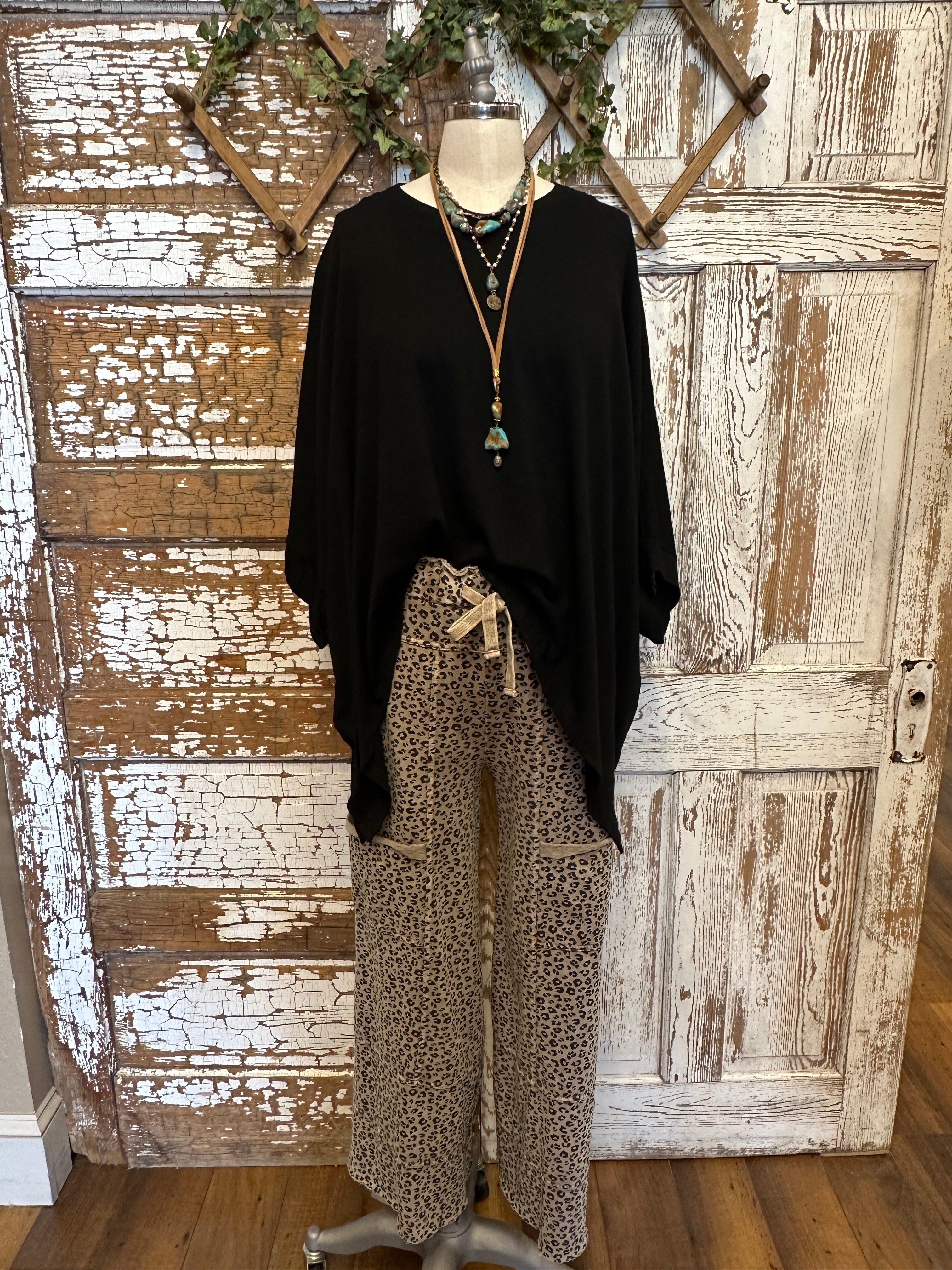 Lu wearing black flowy top and patterned leopard print pants with handmade jewelry in a rustic boutique springfield, mo