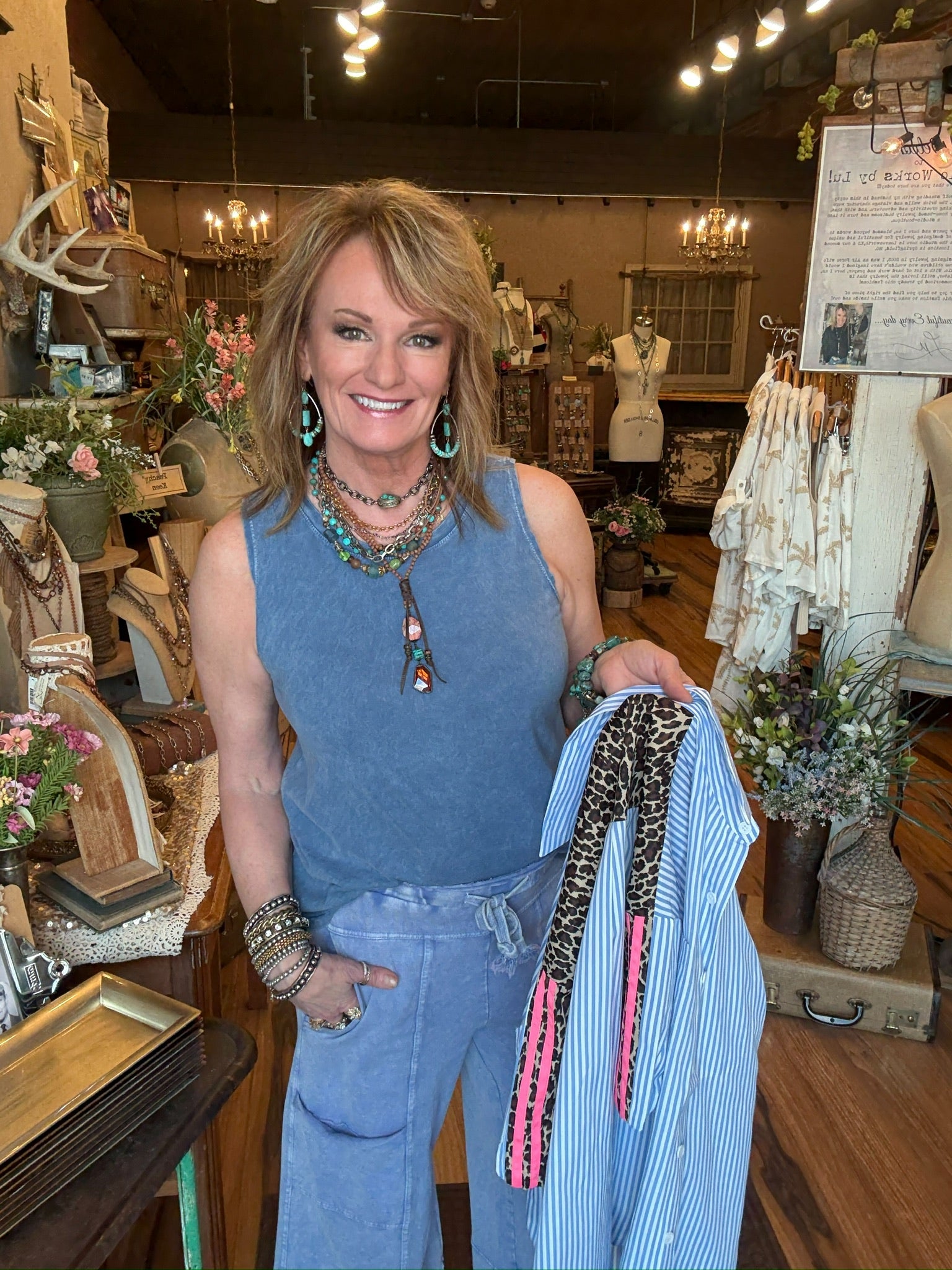 Lu holding leopard and pink accented blue striped shirt with leisure pants in her boutique clothing and jewelry store 