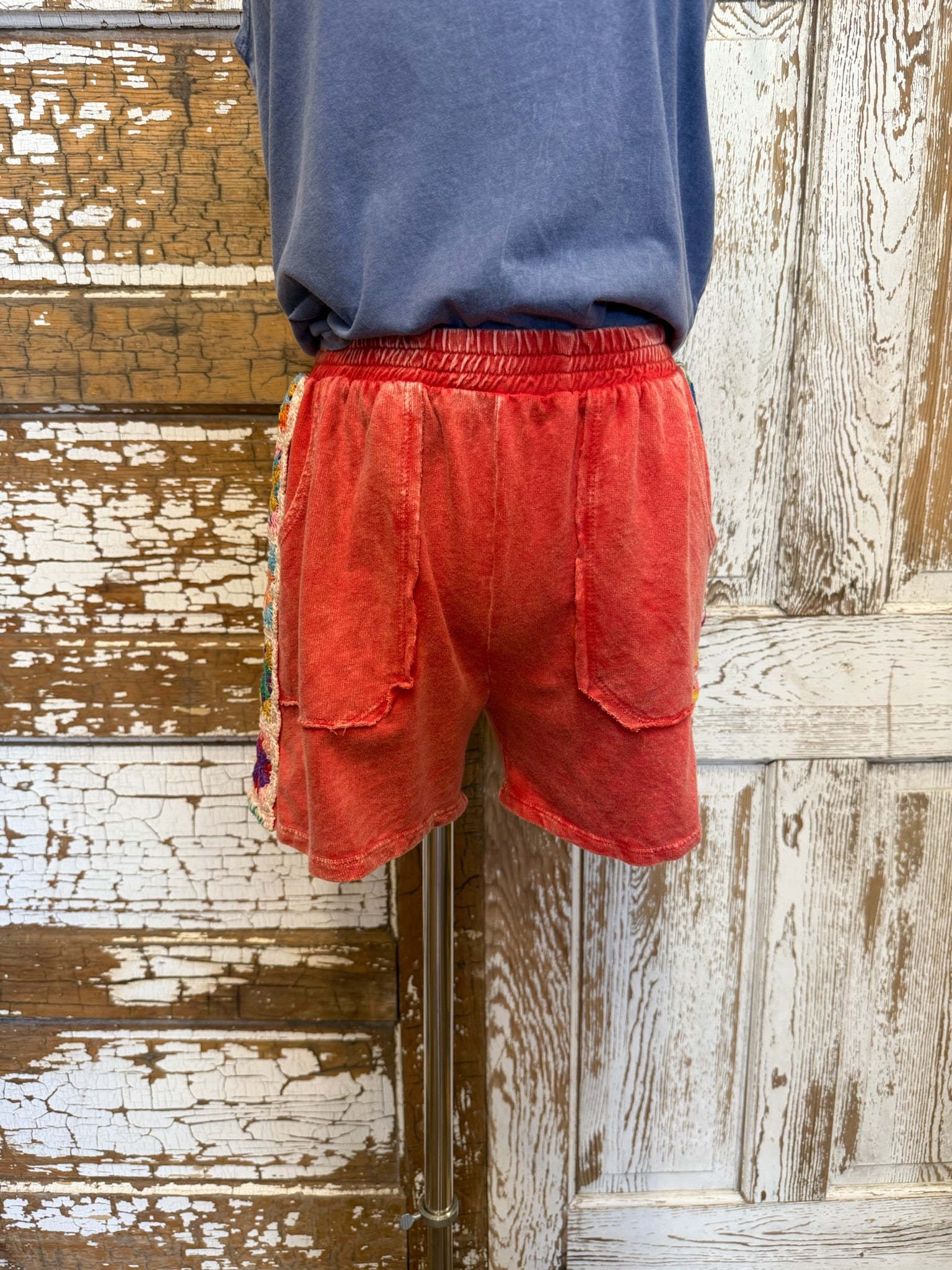 Person wearing red shorts and a blue shirt standing against a wooden wall.