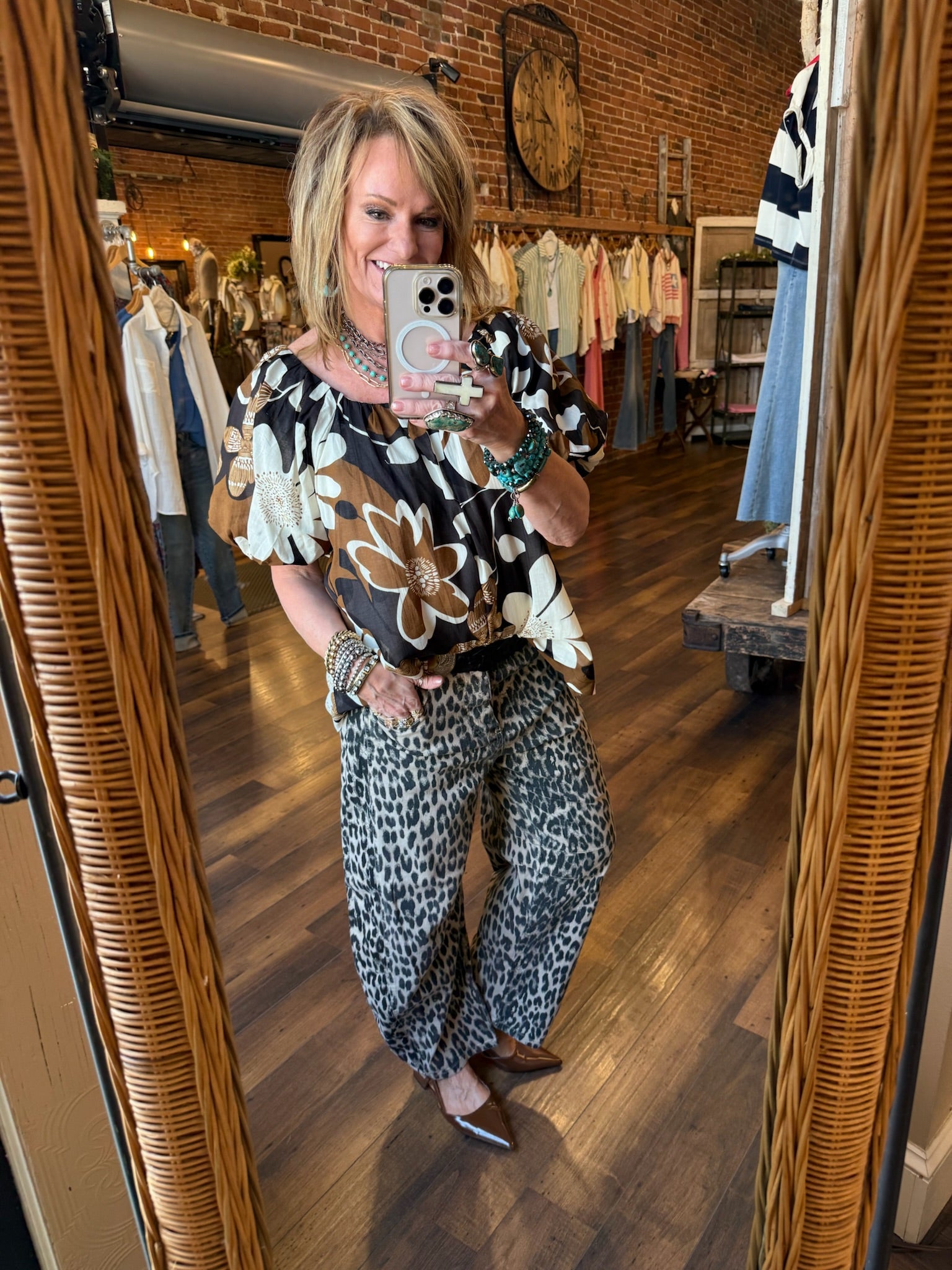 Lu taking a mirror selfie in Leavenworth, KS boutique wearing a floral top and leopard print barrel pants wearing turquoise jewelry. 